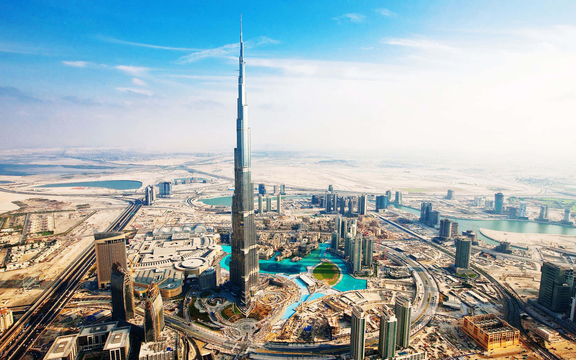 Burj Khalifa 桌布 壁紙 — 杜拜天際線的航拍圖，哈里發塔聳立於現代摩天大樓和沙漠景觀之上，天空湛藍明亮。