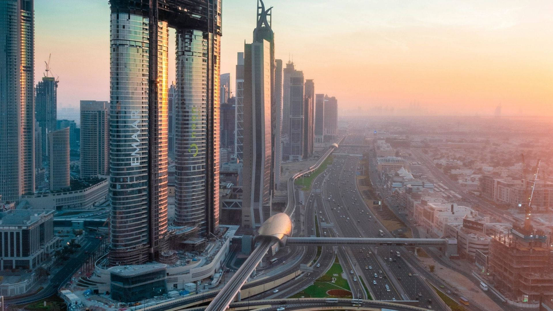 Dubai 桌布 壁紙 — 杜拜天際線的鳥瞰圖，夕陽西下，高聳的摩天大樓和繁忙的高速公路沐浴在金色光芒中。