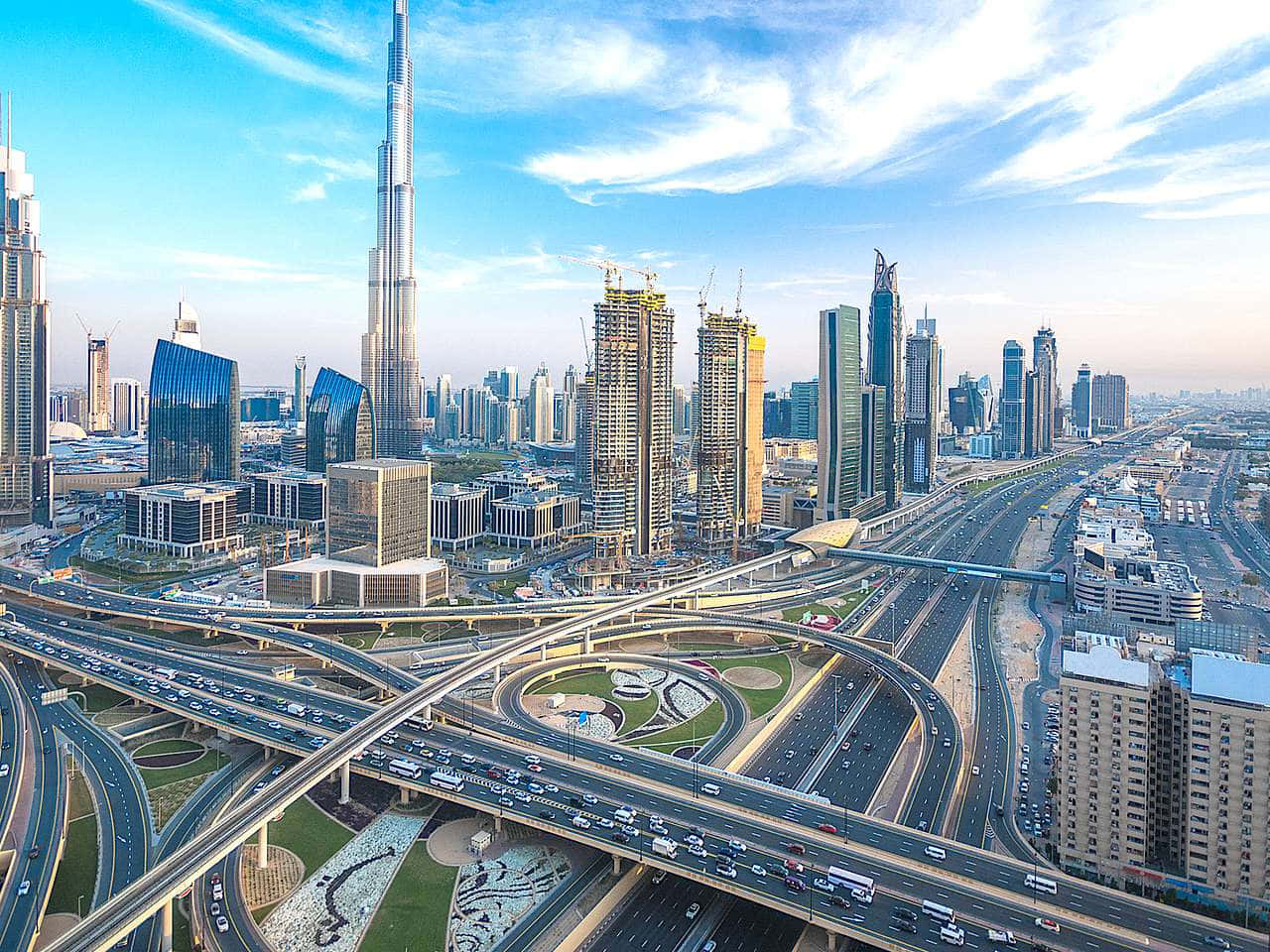 Burj Khalifa 桌布 壁紙 — 杜拜未來主義天際線的航拍圖，在明亮的藍天下，哈里發塔聳立在複雜的高速公路交匯處之上。