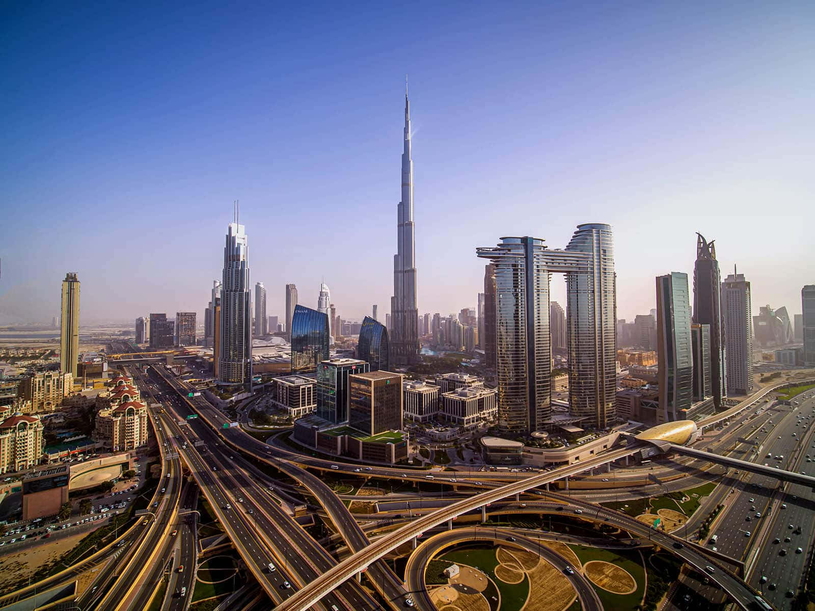 Burj Khalifa 桌布 壁紙 — 杜拜未來主義天際線的鳥瞰圖，以哈里發塔和錯綜複雜的高速公路網絡為主，在晴朗的藍天下。