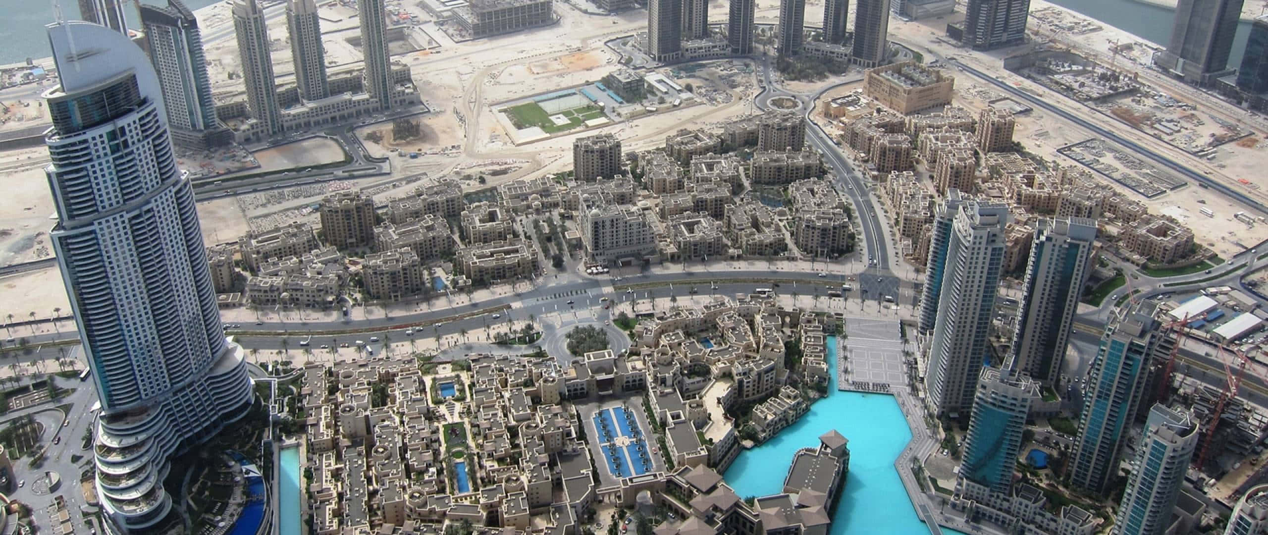 Uae 桌布 壁紙 — 杜拜未來主義天際線的鳥瞰圖，高聳的摩天大樓和綠松石色的人工運河蜿蜒穿過密集的城市發展。