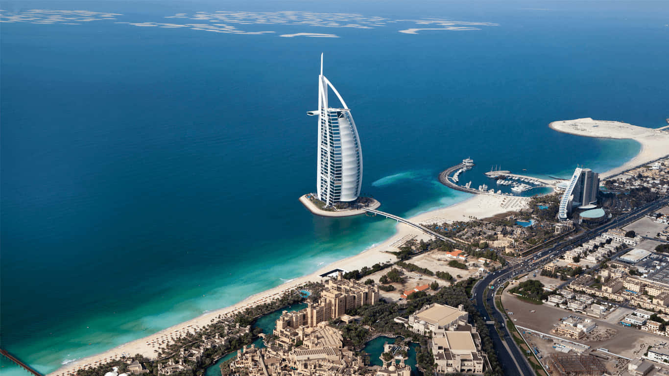 海灘 桌布 壁紙 — 杜拜標誌性帆船酒店（Burj Al Arab）的航拍圖，酒店獨自矗立於人工島上，四周環繞著碧綠海水和城市景觀。