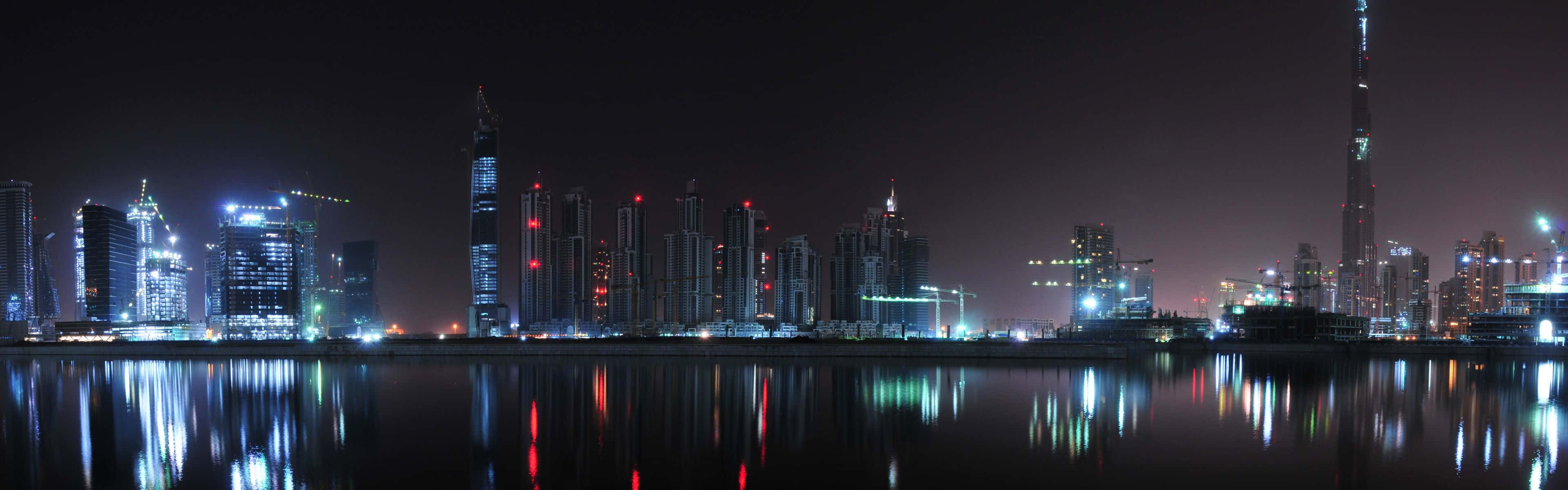 2 Monitor 桌布 壁紙 — 杜拜璀璨天際線的 panoramic 夜景，倒映在平靜水面上，哈里發塔高聳突出。