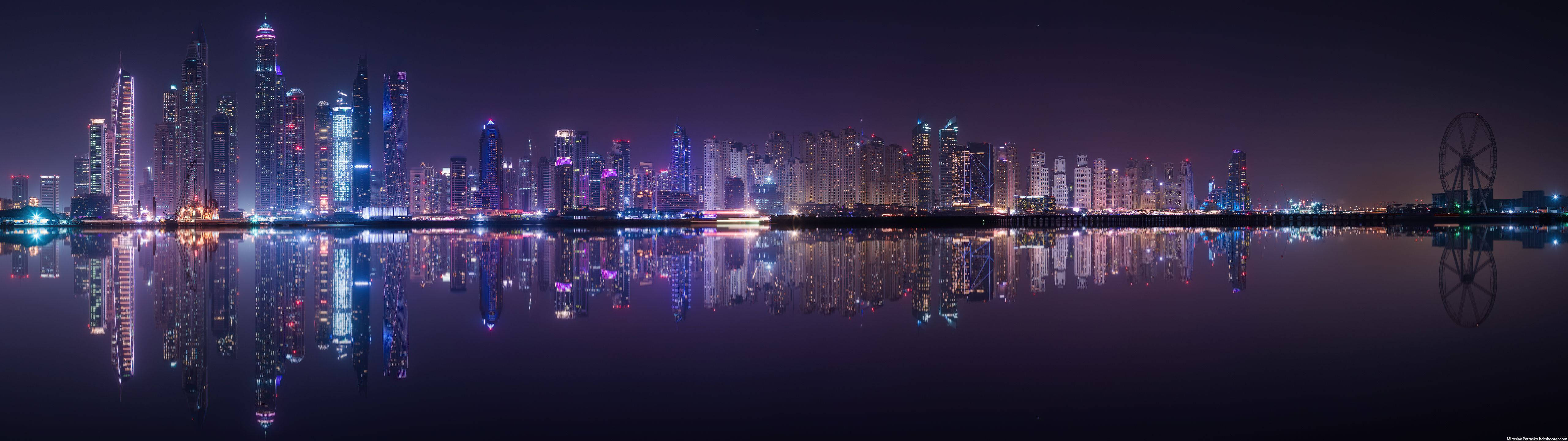 桌布 壁紙 — 杜拜閃爍天際線的 panoramic 夜景，完美倒映在平靜的水面上，右邊有一個摩天輪。