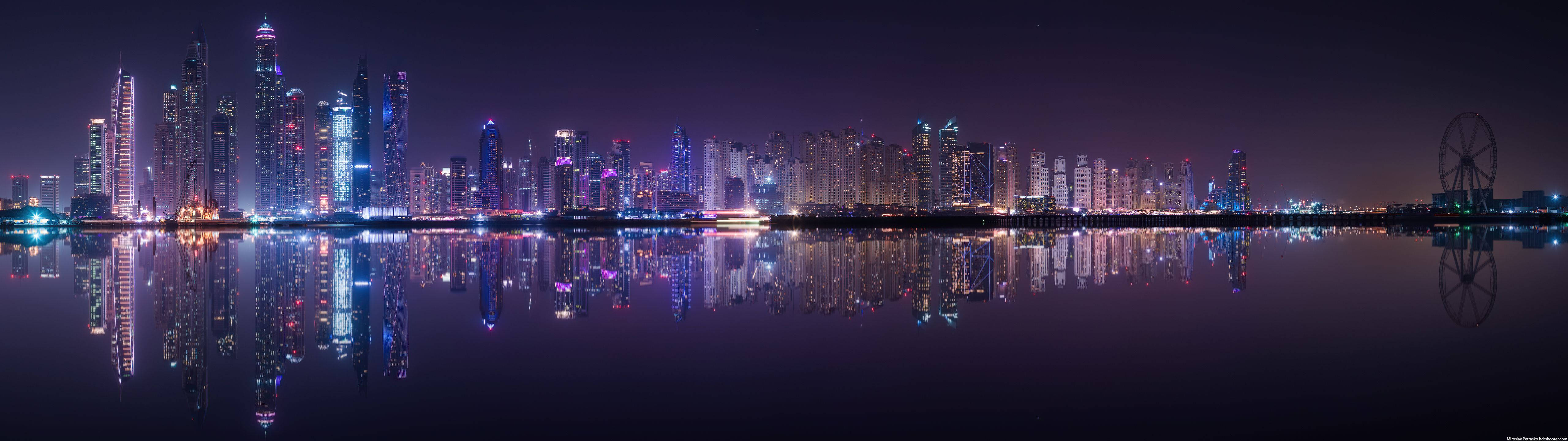 夜晚的杜拜天際線，摩天大樓和摩天輪倒映在水中。 — 超寬 GIF 壁紙
