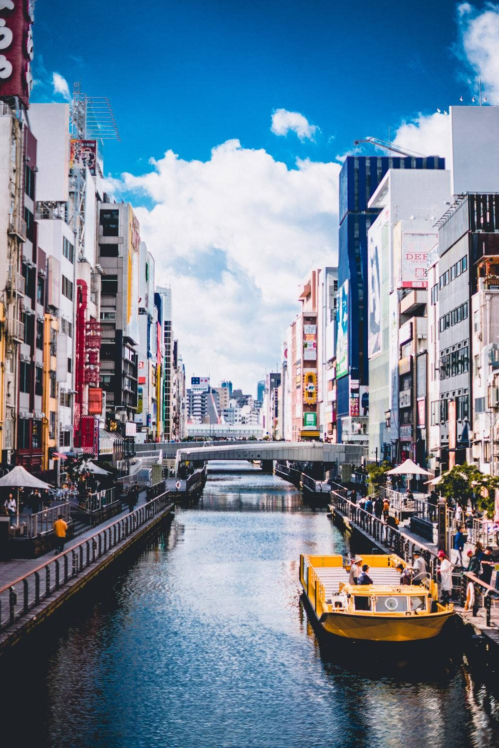 黃色運河船載著乘客在陽光明媚的天空下穿過繁忙的東京城市景觀。