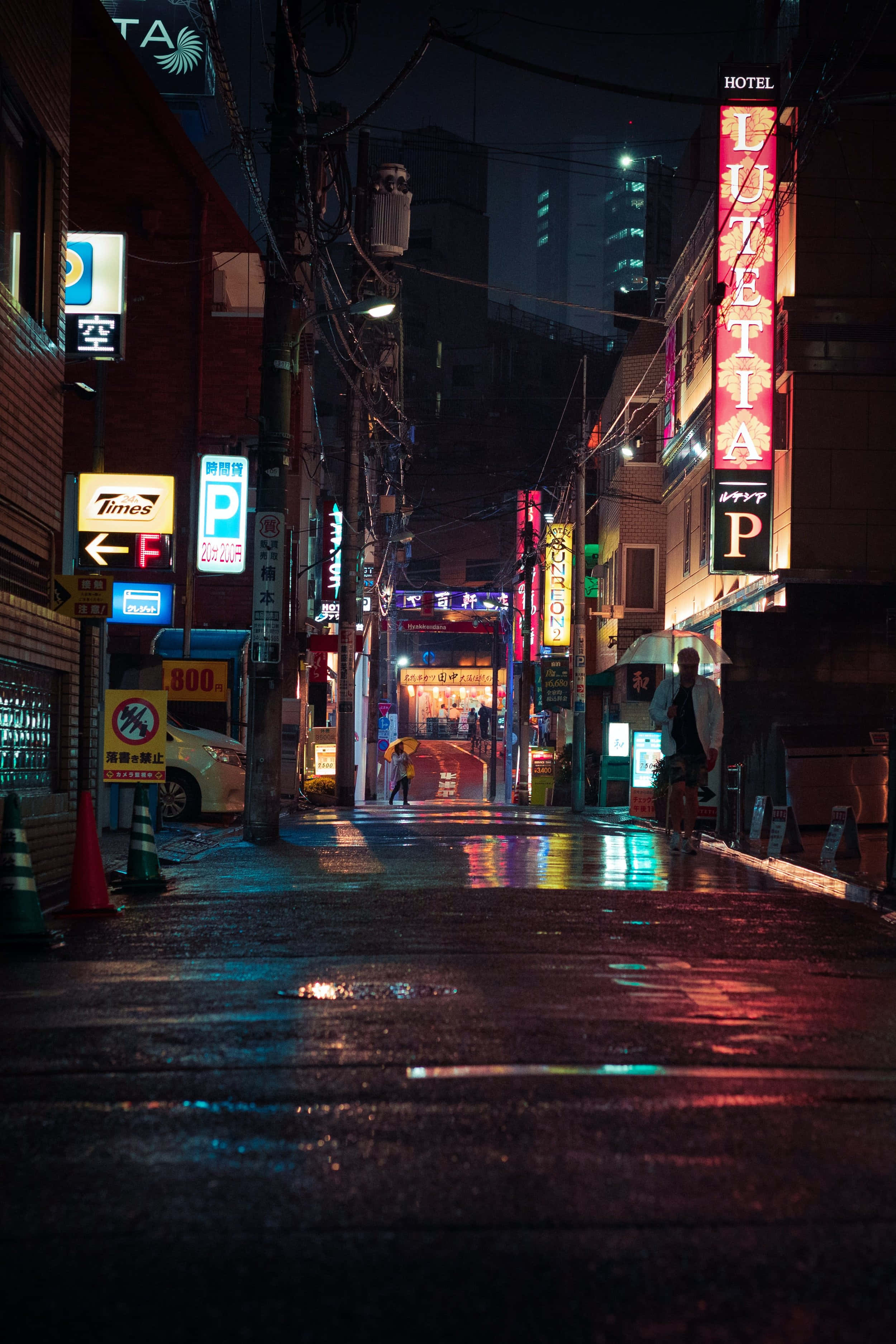 夜晚 桌布 壁紙 — 東京一條被雨水打濕、霓虹燈照亮的後巷，在夜晚昏暗的路燈下，將鮮豔的招牌反射在濕漉漉的路面上。