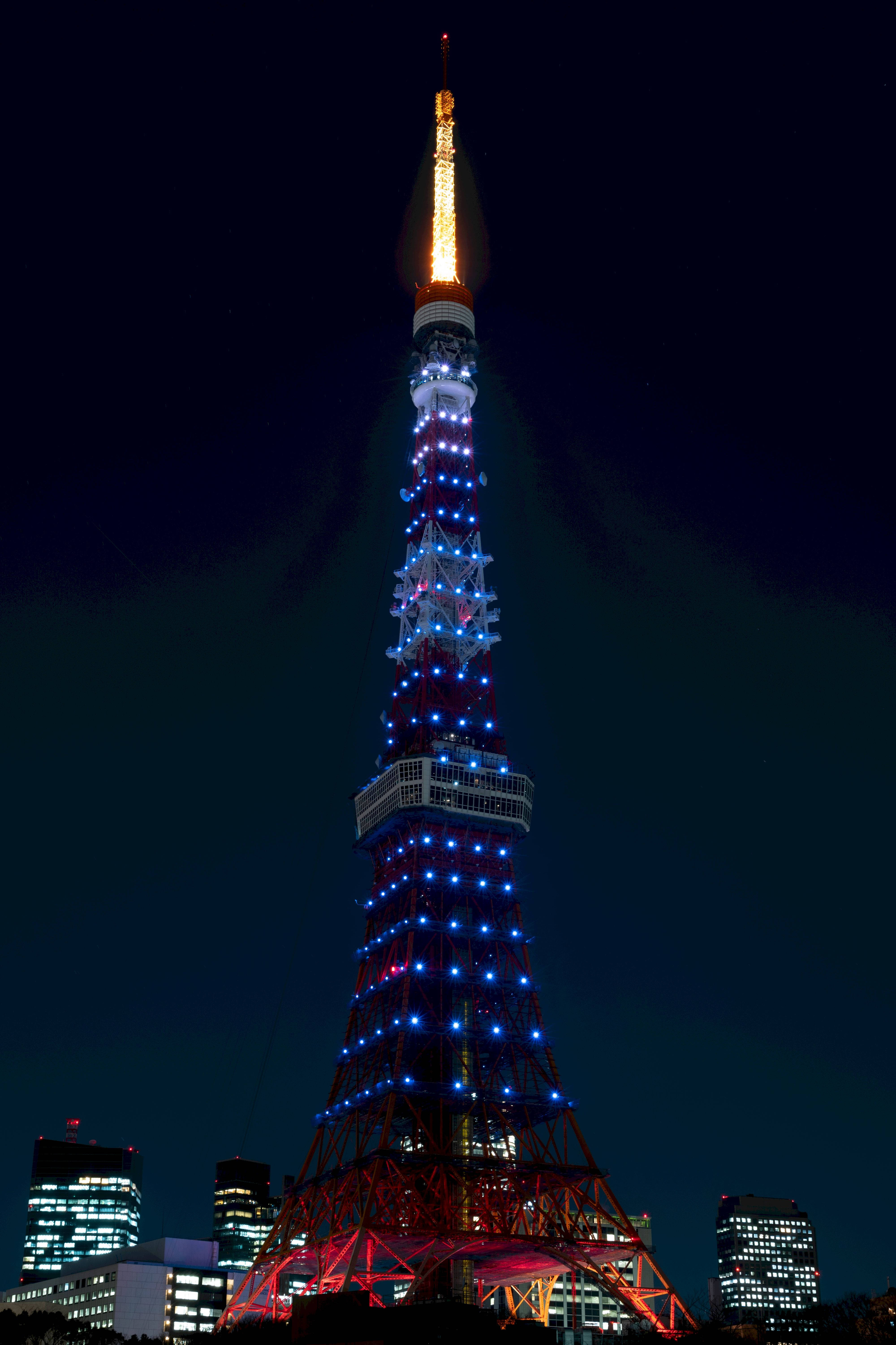 日本 桌布 壁紙 — 東京塔以紅、藍、金色燈光點亮，背景是漆黑的夜空和城市建築。