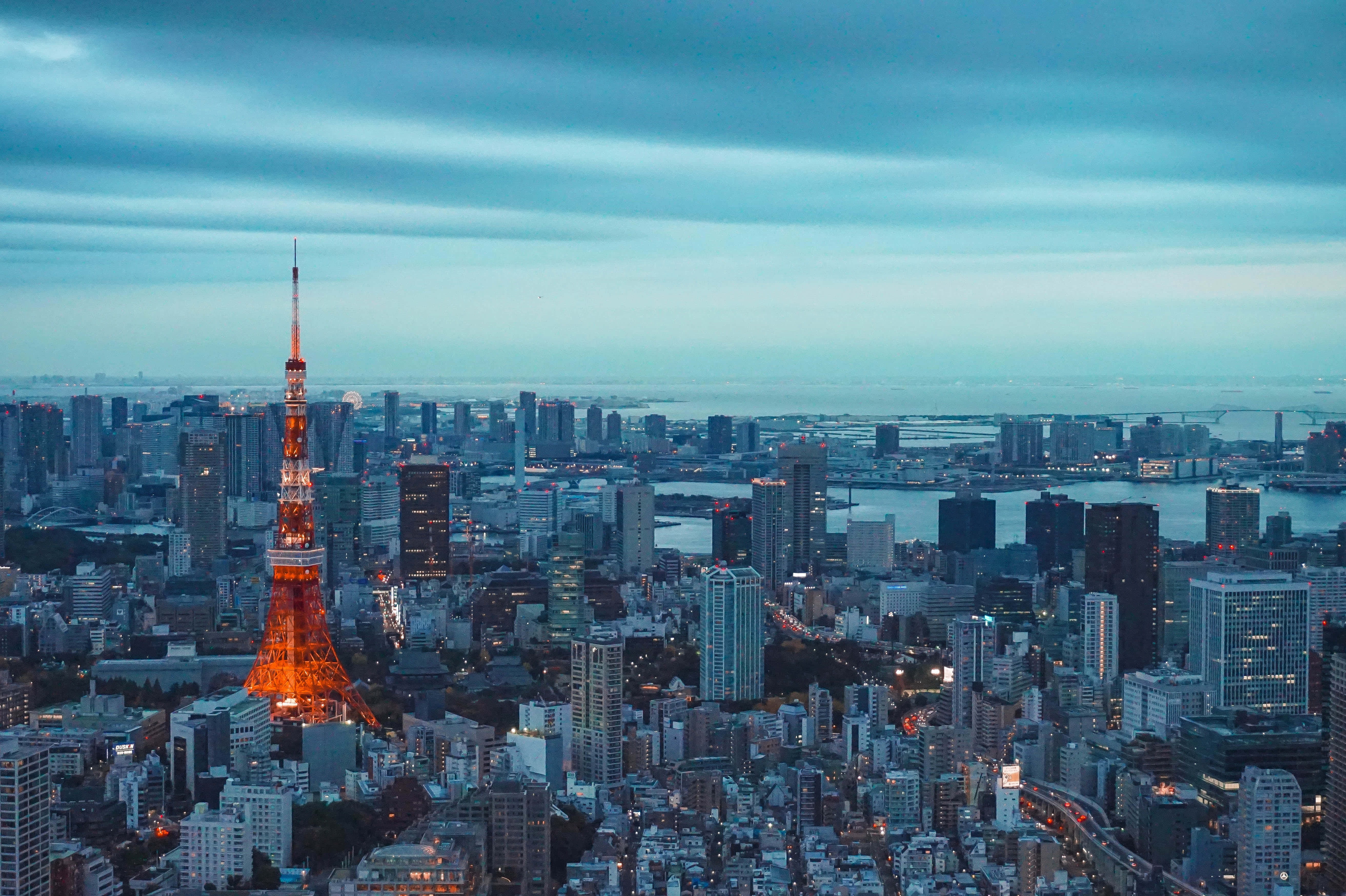 日本 桌布 壁紙 — 東京塔在昏暗的藍天下溫暖地發光，城市燈光在都市擴展區閃爍。