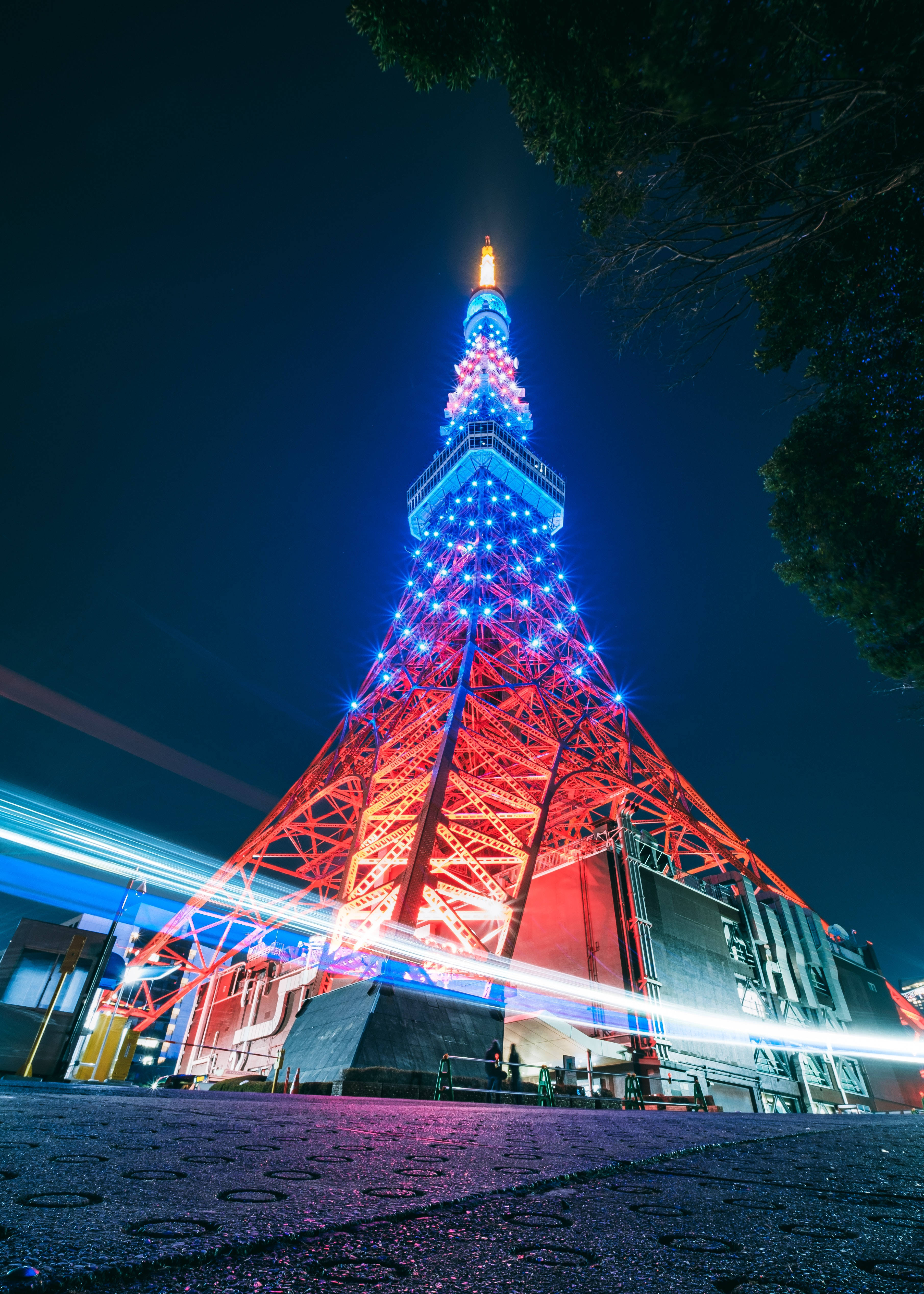 日本 桌布 壁紙 — 東京塔在深沉的夜空中閃耀著鮮豔的紅藍燈光，伴隨著過往車輛留下的光跡。