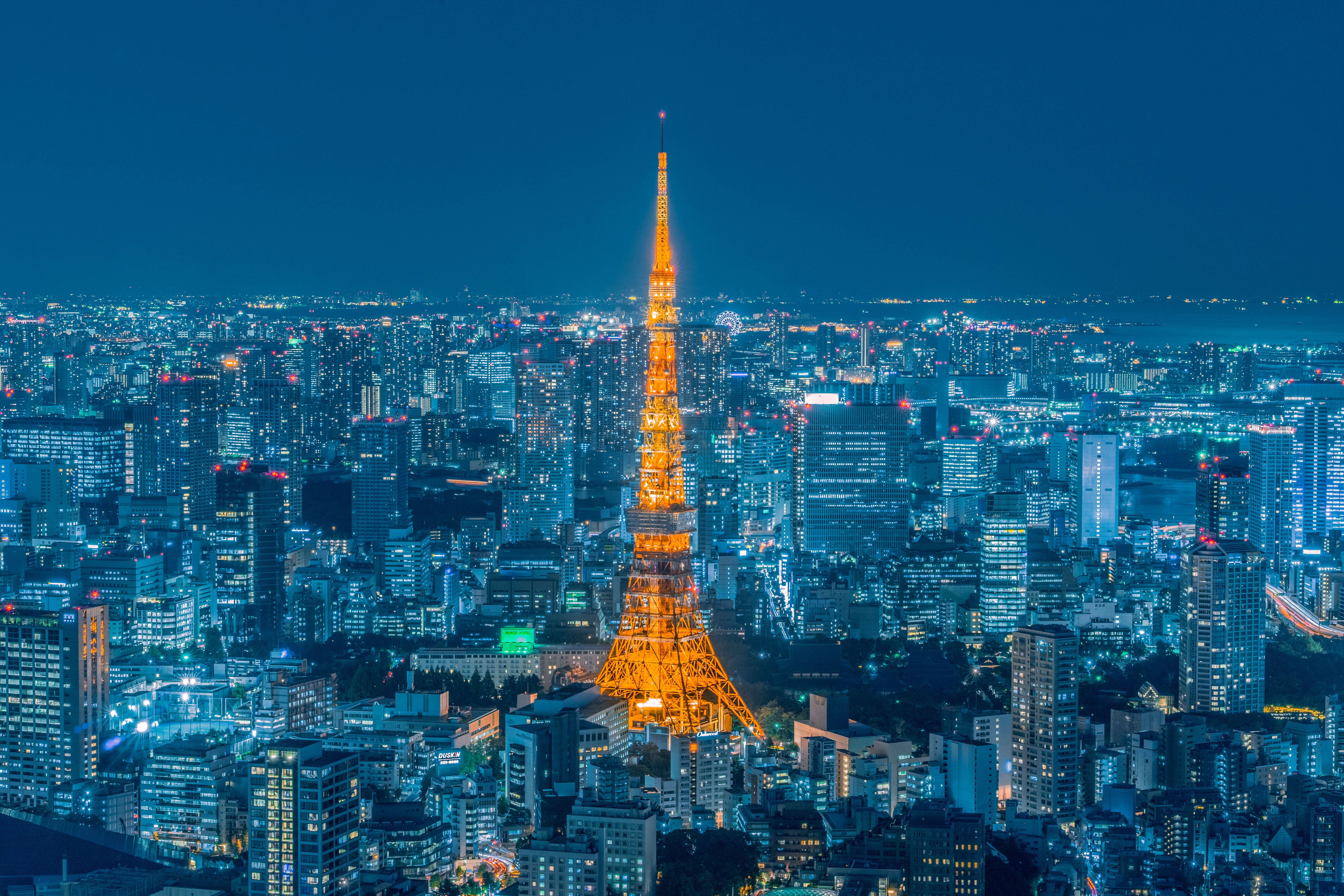 日本 桌布 壁紙 — 東京塔在深藍色夜空下溫暖地發光，下方是廣闊的閃爍城市景觀。