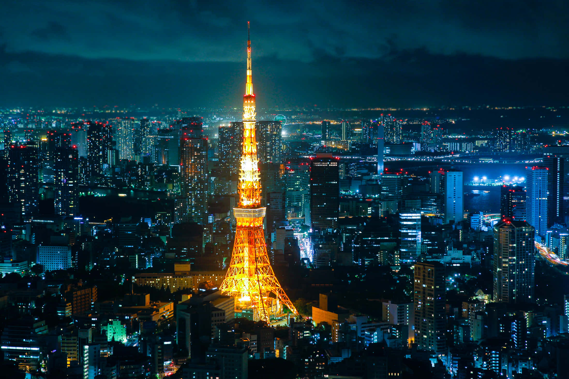 東京鐵塔 桌布 壁紙 — 東京塔在黑暗的天空中溫暖地發光，照亮了下方夜晚廣闊的霓虹燈城市景觀。