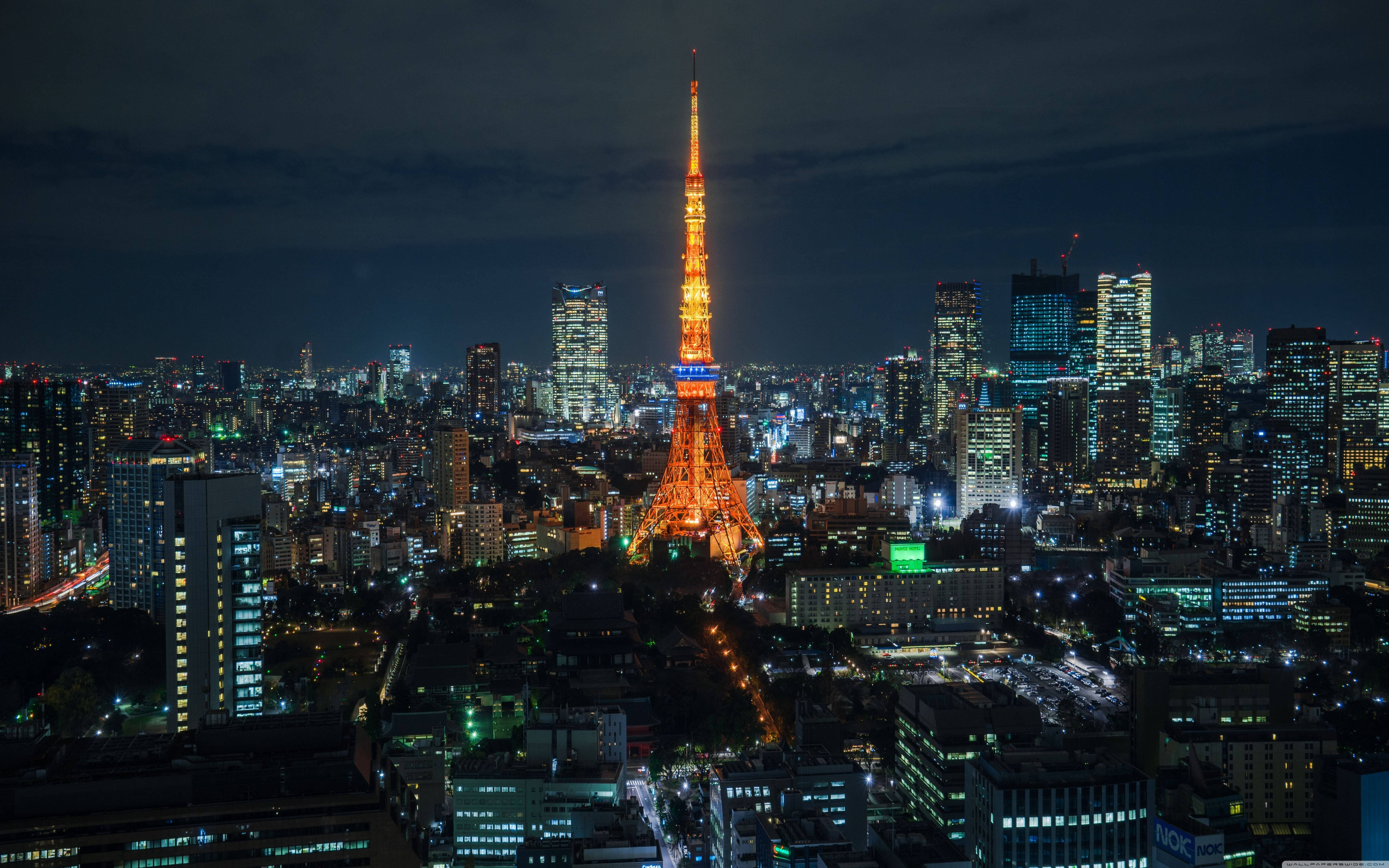 東京 桌布 壁紙 — 東京塔在黑暗的天空中溫暖地發光，城市燈光照亮了下方廣闊的城市景觀。