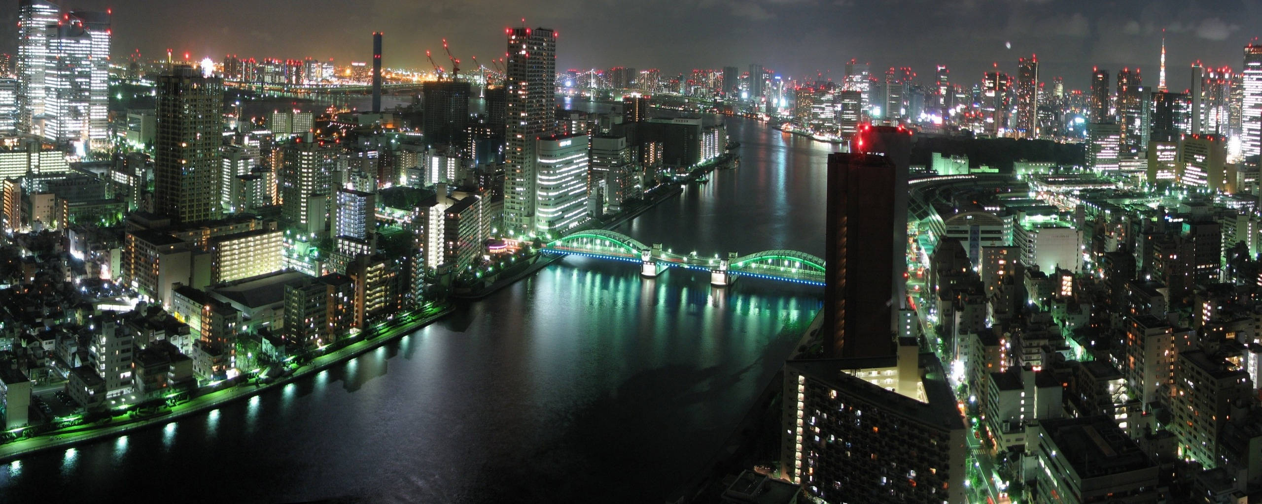 high 桌布 壁紙 — 東京夜晚閃爍天際線的空中景觀，河流與照明橋樑穿過密集的城市建築。
