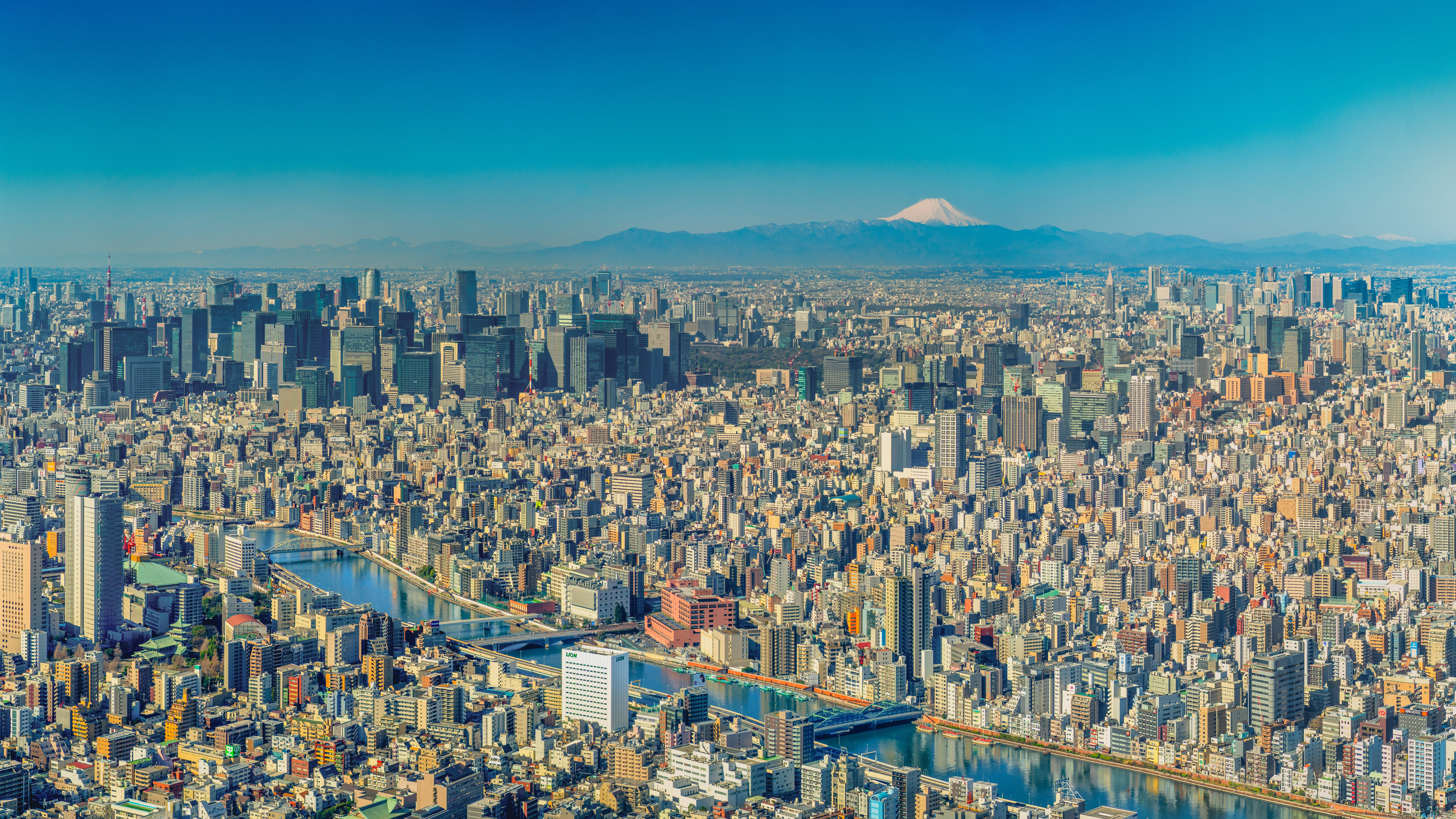 富士山 桌布 壁紙 — 東京天際線的鳥瞰圖，遠處富士山白雪覆蓋的山峰在晴朗的藍天下升起。
