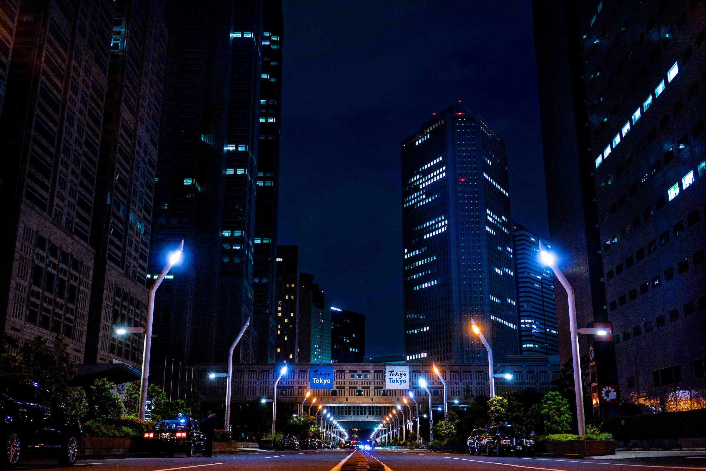 夜空 桌布 壁紙 — 東京的夜景，高聳的摩天大樓在街燈下閃耀，道路延伸至遠方。