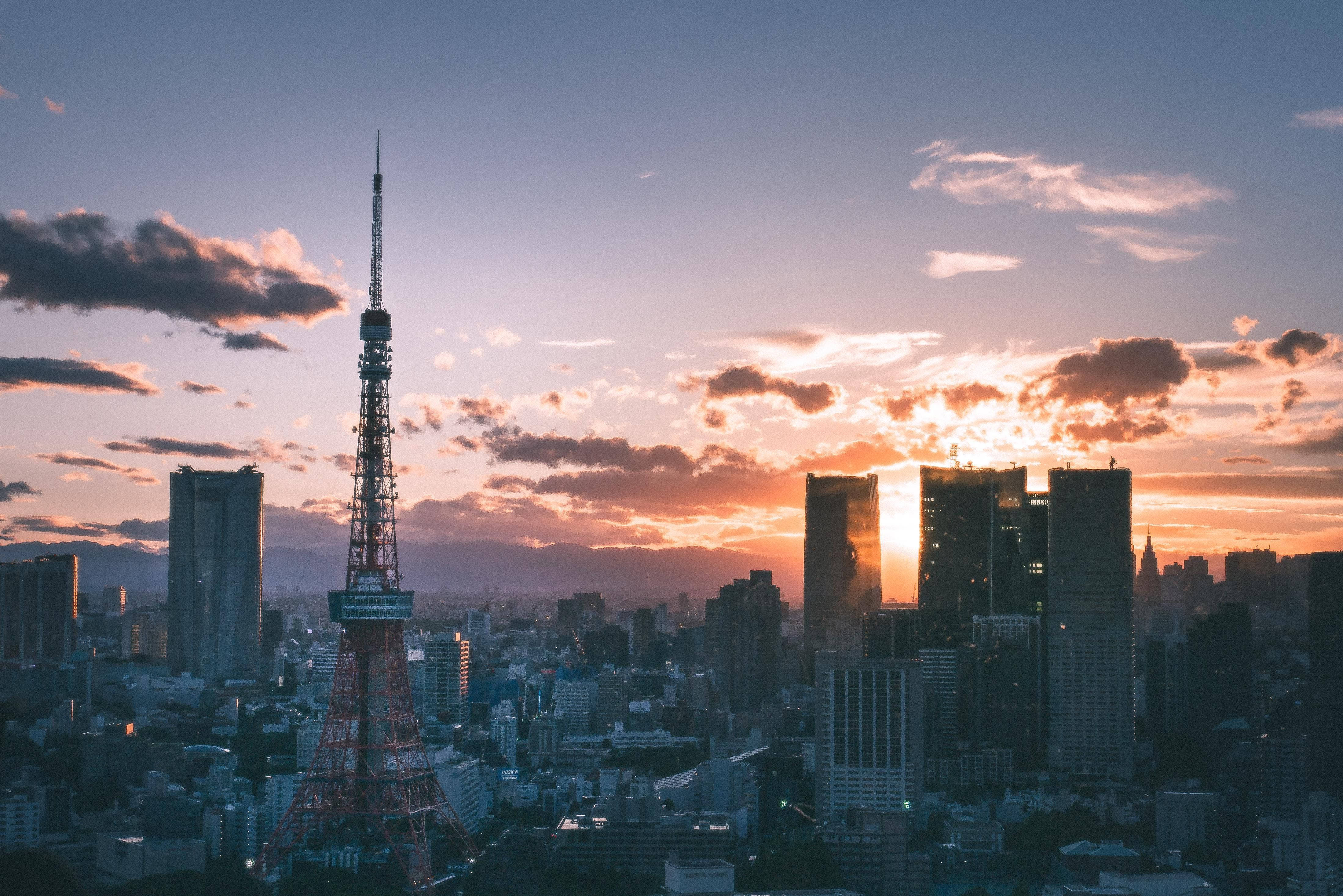 Fukuoka 桌布 壁紙 — 東京鐵塔在充滿活力的日落天空下高聳矗立，伴隨著橙色的雲彩和剪影般的摩天大樓。
