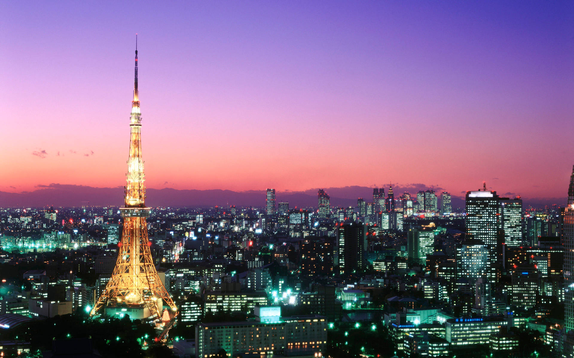 日本 桌布 壁紙 — 東京鐵塔在充滿活力的紫色和粉紅色暮色天空中閃耀著金色光芒，下方是廣闊的燈火通明的摩天大樓城市景觀。