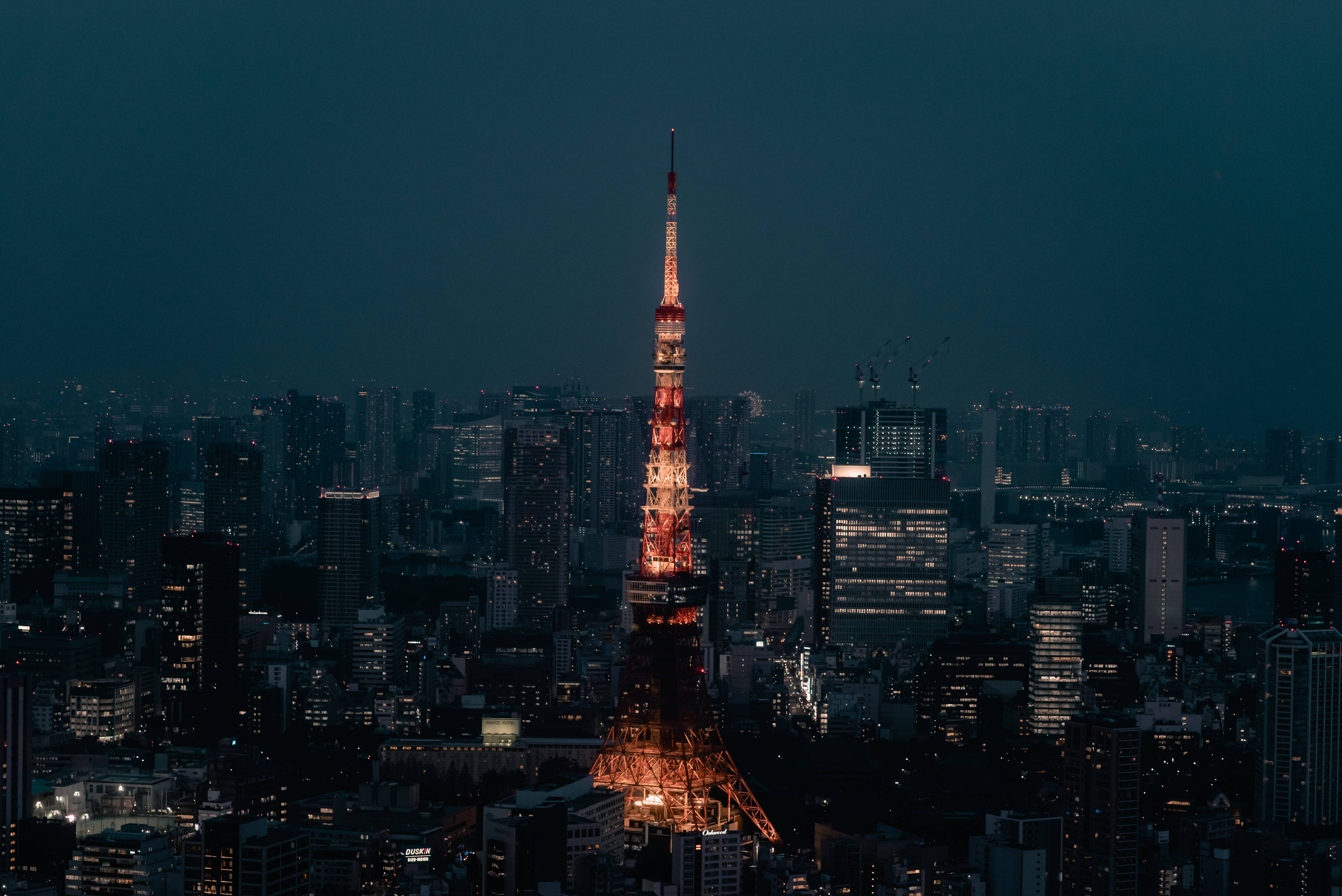 日本 桌布 壁紙 — 東京鐵塔在夜晚黑暗的城市景觀中溫暖地發光，周圍的摩天大樓被環境城市燈光照亮。