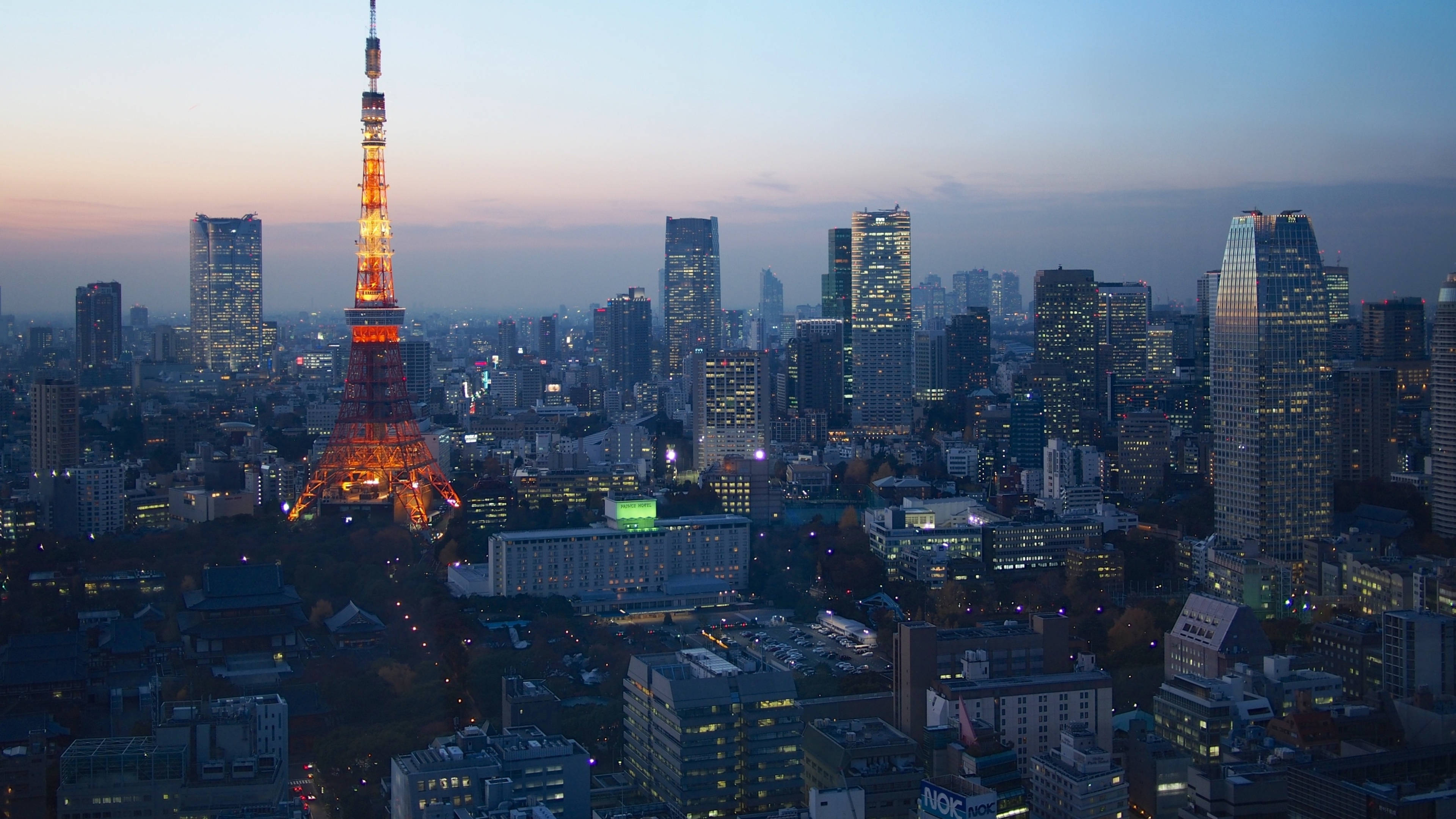 日本 桌布 壁紙 — 東京鐵塔在暮色天空中溫暖地發光，城市燈光照亮了下方的城市天際線。