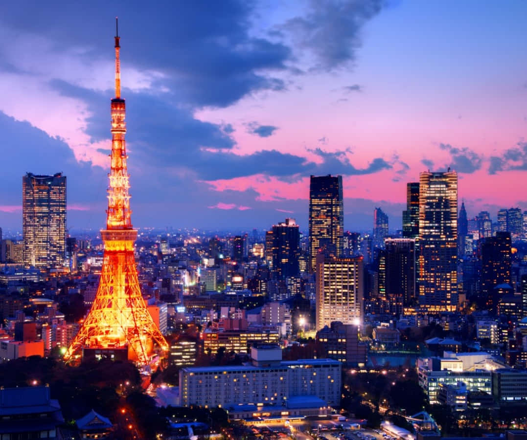 東京 桌布 壁紙 — 東京鐵塔在暮色天空中溫暖地發光，天空佈滿粉紅和紫色的雲彩，下方是燈火通明的摩天大樓天際線。