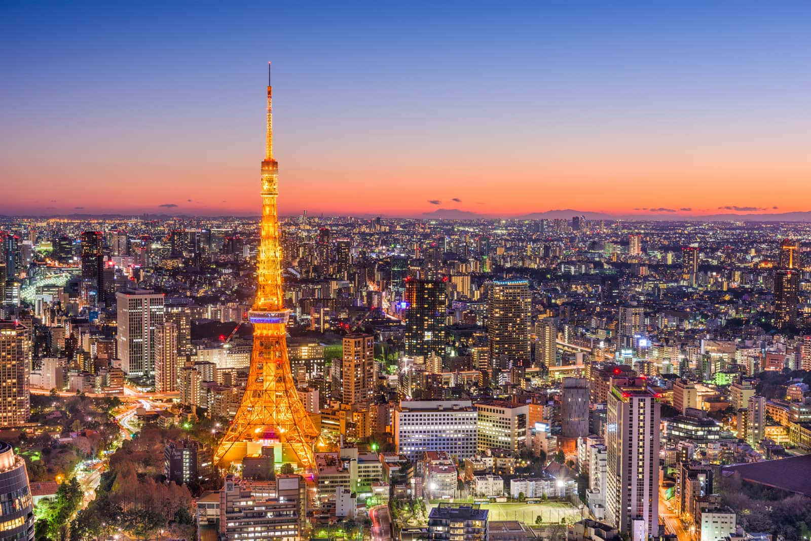 Tokyo Japan 桌布 壁紙 — 東京鐵塔在暮色天空中閃耀金光，城市燈光照亮下方廣闊的大都會。