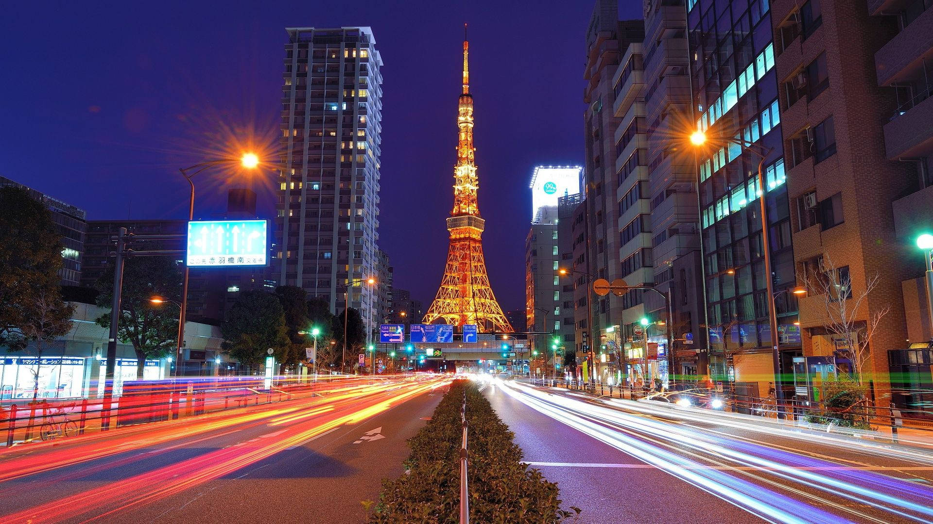 日本 桌布 壁紙 — 東京鐵塔在暮色天空中閃耀金光，汽車燈光的條紋模糊地穿過城市街道。