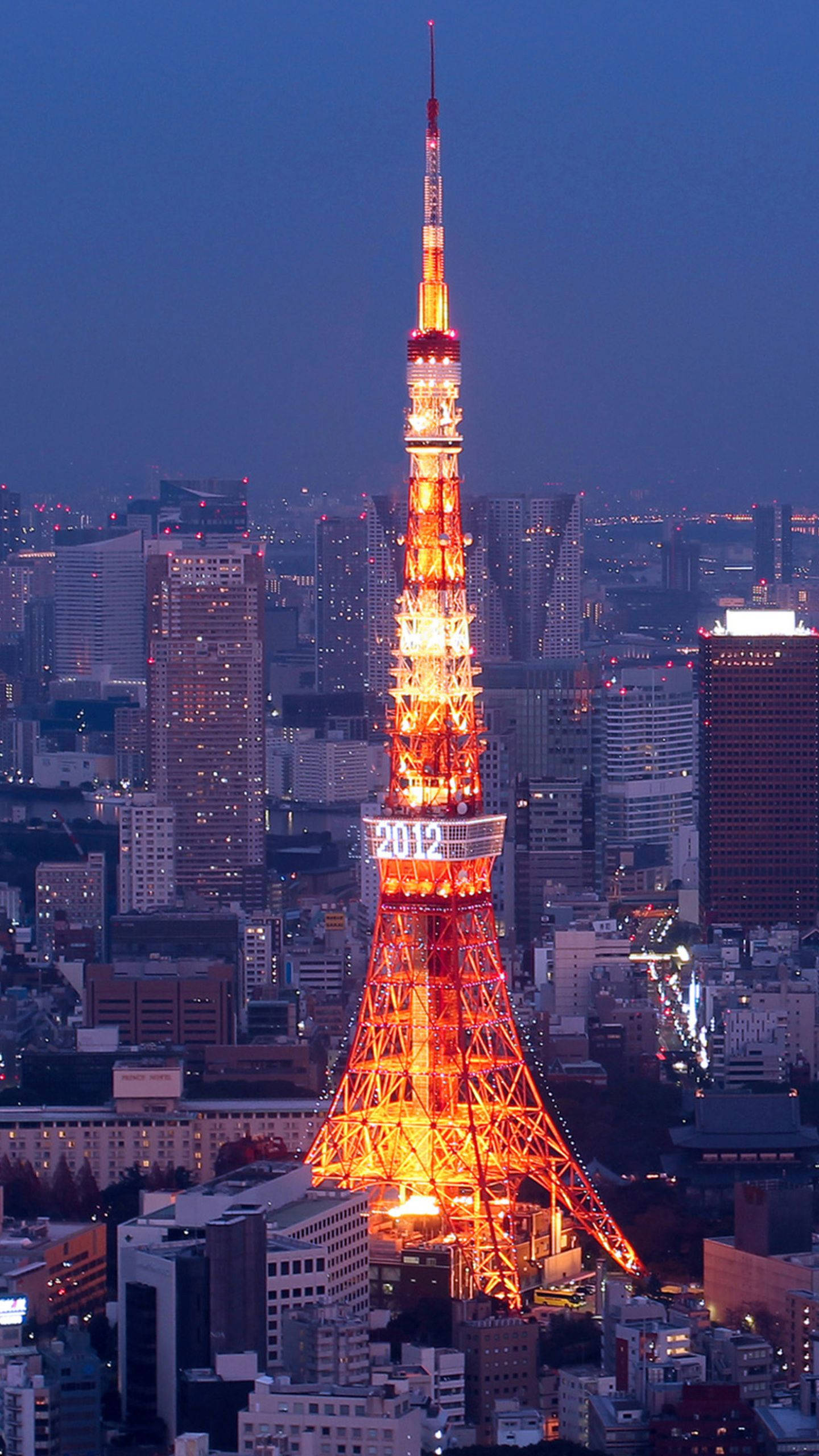 日本 桌布 壁紙 — 東京鐵塔在深藍色暮色天空下，於廣闊的摩天大樓城市景觀之上溫暖地發光。