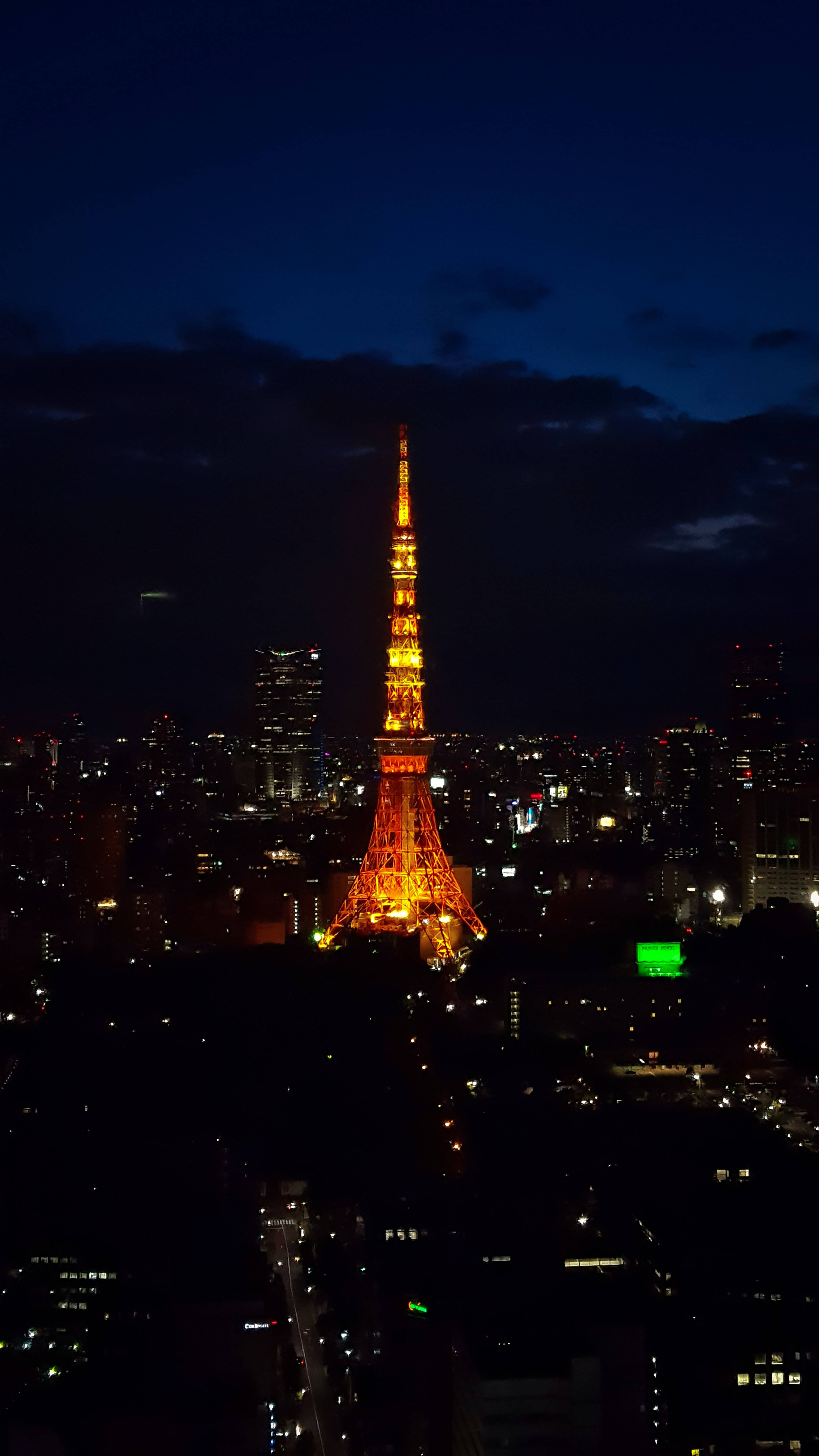 日本 桌布 壁紙 — 東京鐵塔在深藍色的夜空下溫暖地發光，下方是閃爍燈光延伸的城市景觀。