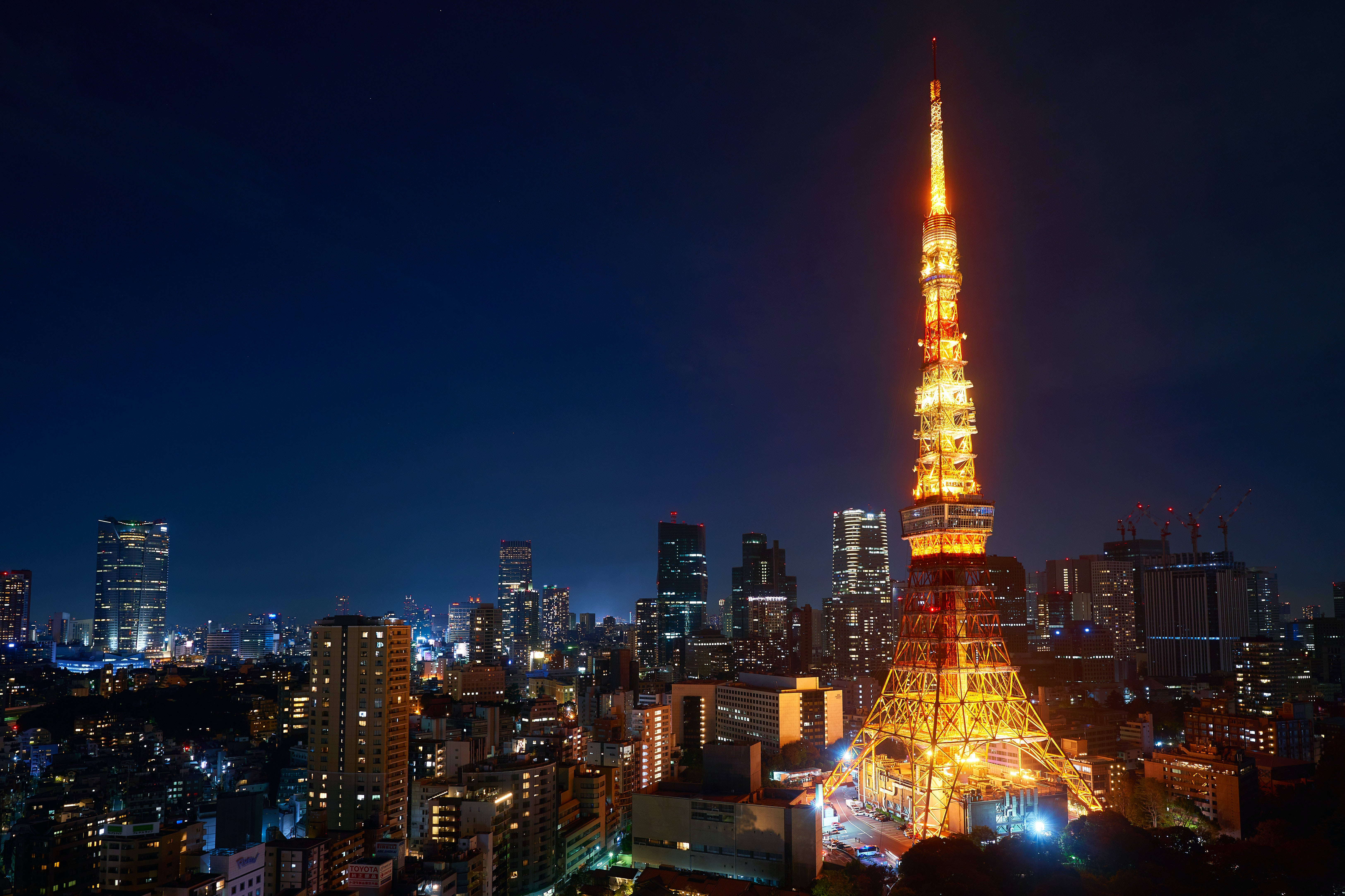 日本 桌布 壁紙 — 東京鐵塔在深藍色的夜空中溫暖地發光，下方是燈火通明的摩天大樓城市景觀。