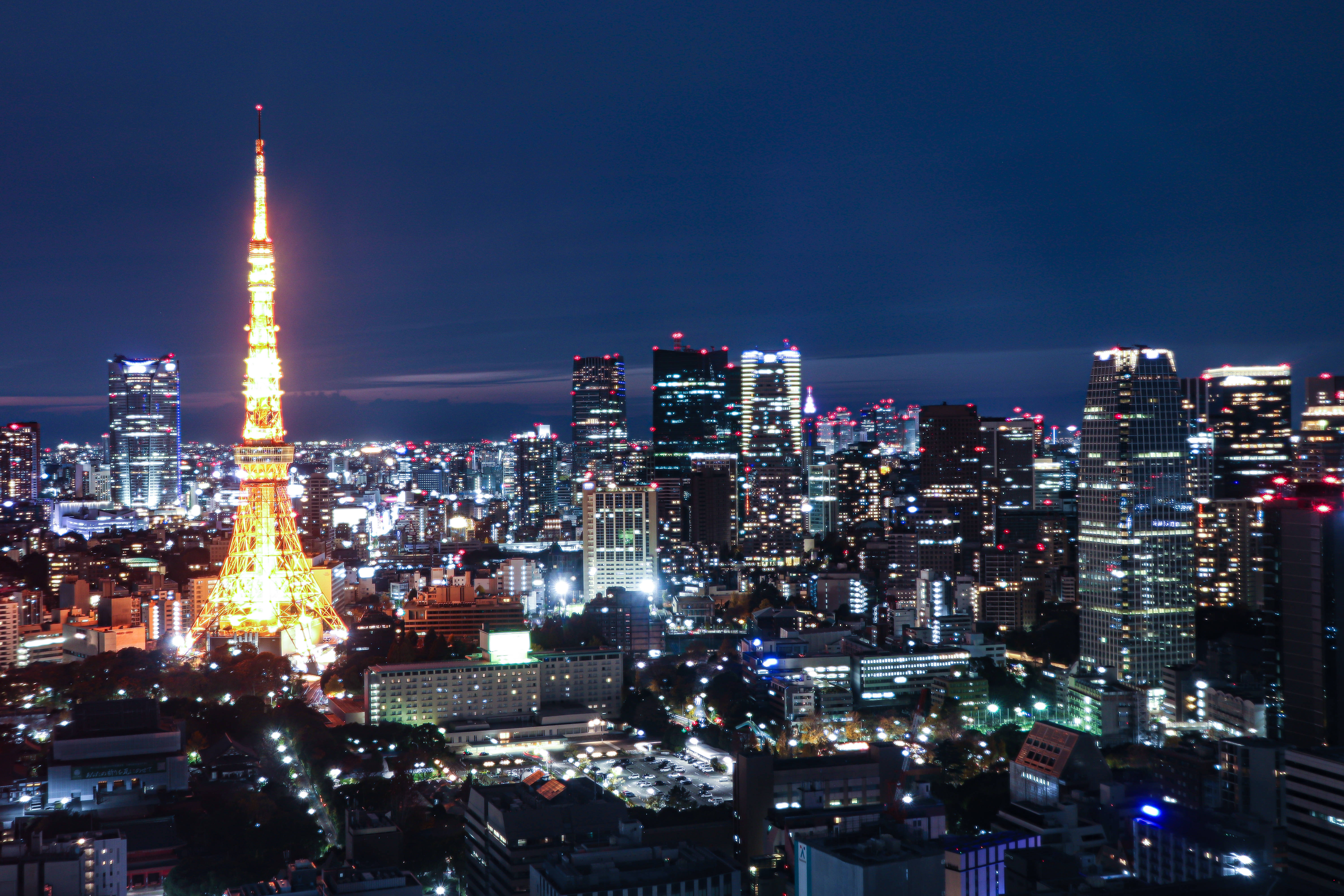 Cyber 桌布 壁紙 — 東京鐵塔在深藍色的夜空中閃耀著金色光芒，城市燈光照亮了下面的城市景觀。