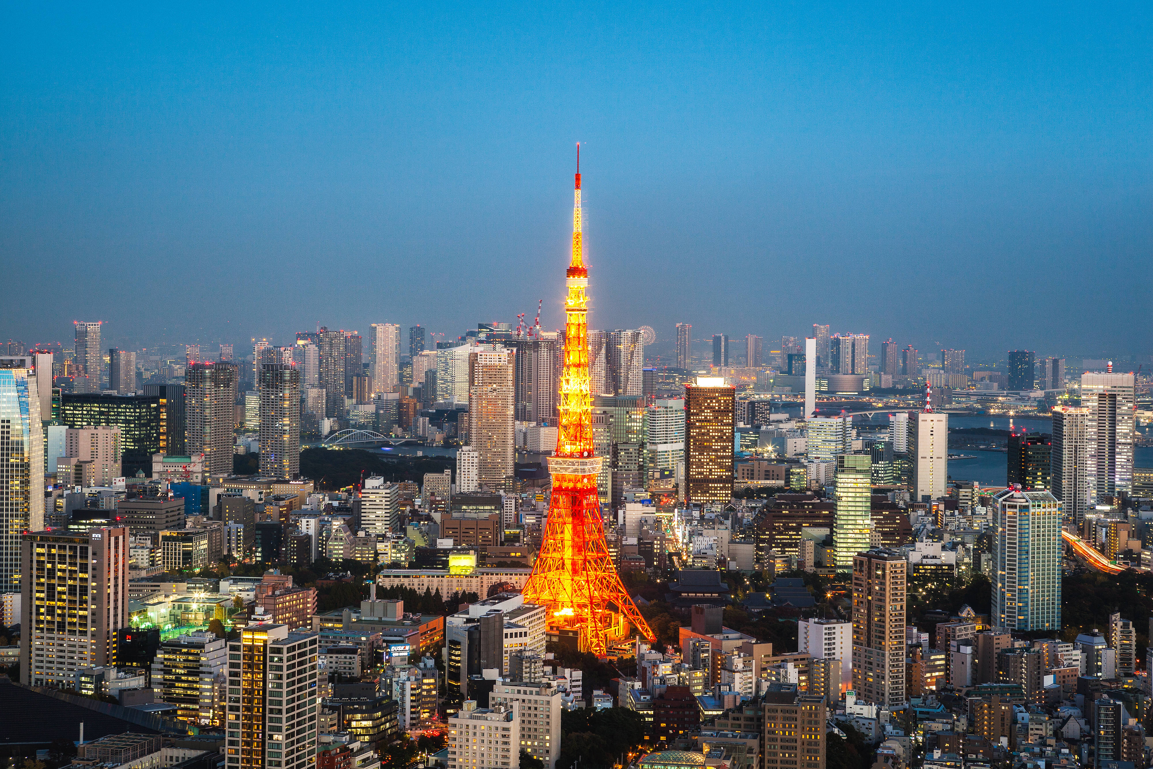 日本 桌布 壁紙 — 東京鐵塔在深藍色的暮色天空中溫暖地發光，下方是廣闊的都市景觀，高樓大廈燈火通明。