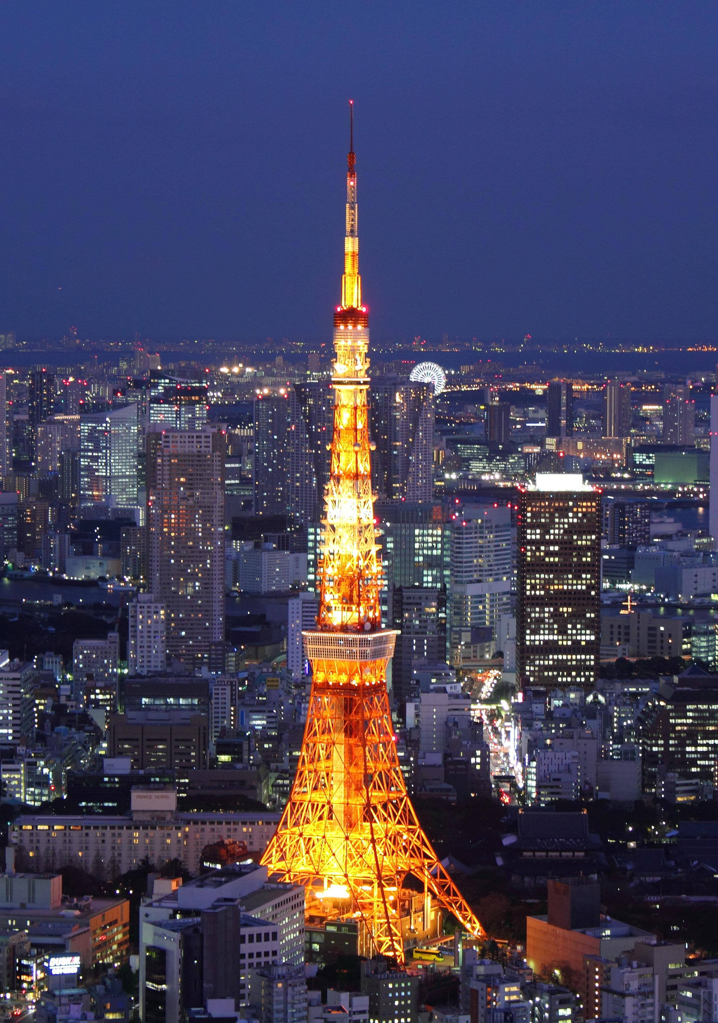 日本 桌布 壁紙 — 東京鐵塔在深藍色的暮色天空中溫暖地發光，下方是廣闊的都市景觀，高樓大廈燈火通明。