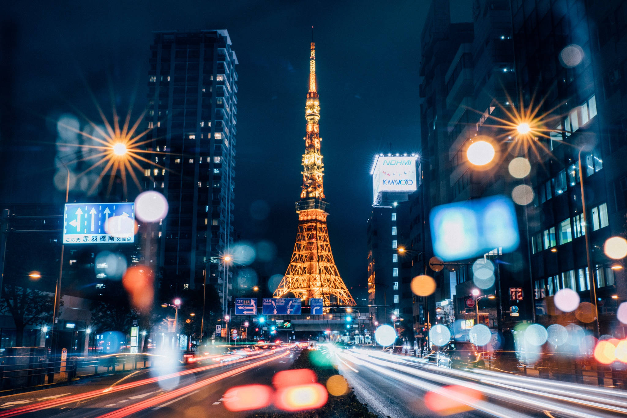 日本 桌布 壁紙 — 東京鐵塔在漆黑的夜空下溫暖地發光，模糊的車燈劃過被雨水弄濕的城市街道。