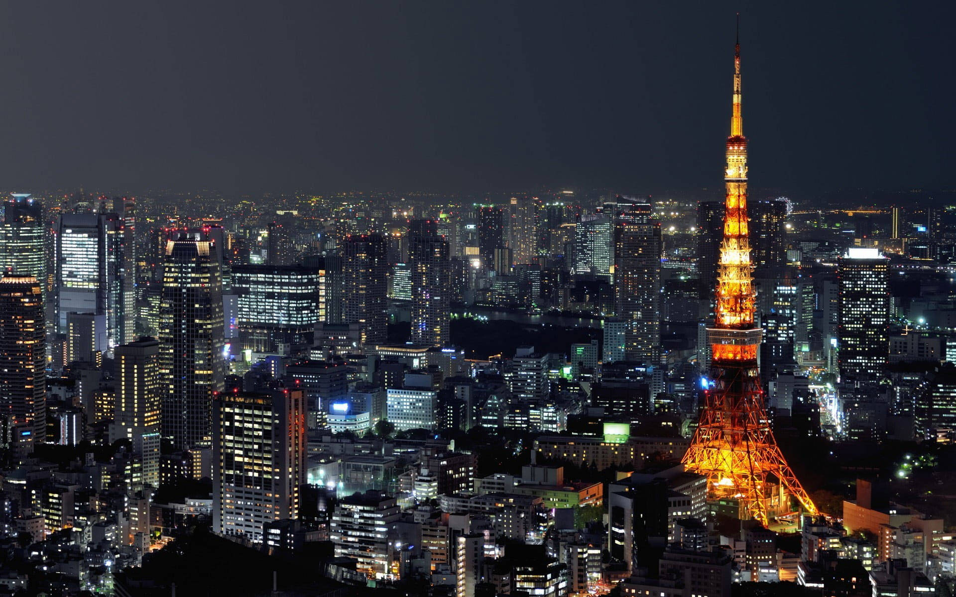 日本 桌布 壁紙 — 東京鐵塔在漆黑的天空中溫暖地發光，城市燈光照亮了下方廣闊的城市景觀。
