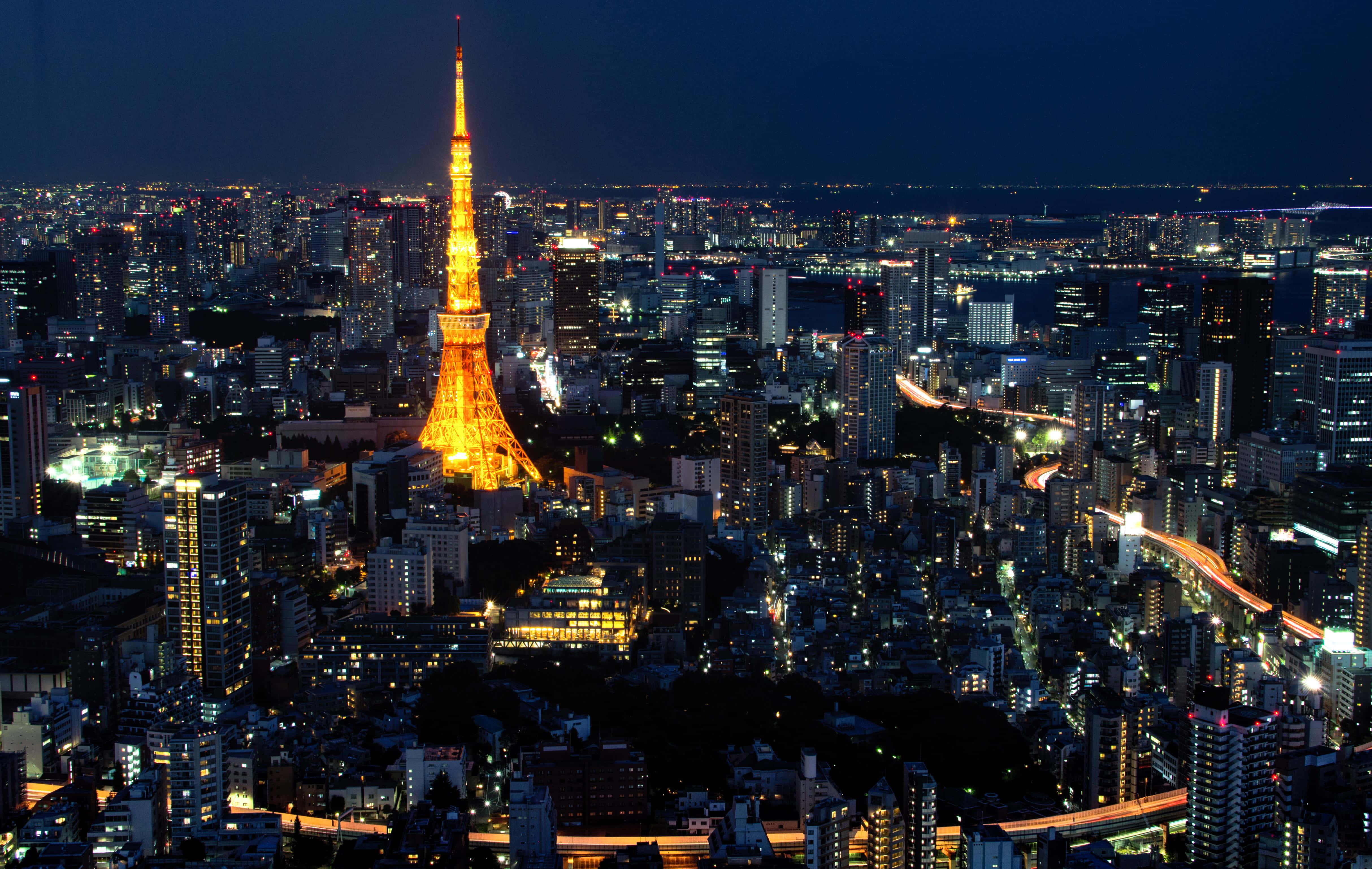 東京鐵塔 桌布 壁紙 — 東京鐵塔在漆黑的天空中閃耀著金色光芒，城市的燈光照亮了下方廣闊的城市景觀。