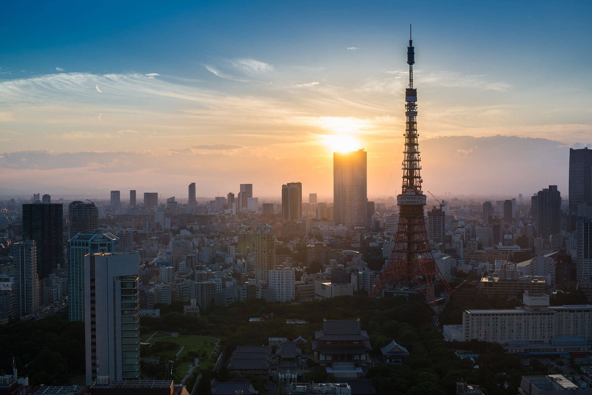 日本 桌布 壁紙 — 東京鐵塔在金色夕陽天空下高聳，俯瞰著擁有現代摩天大樓和傳統屋頂的廣闊城市天際線。