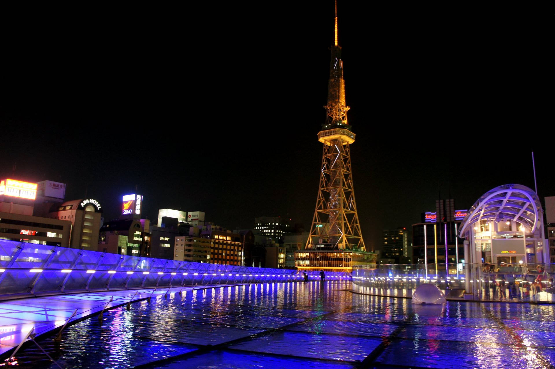 Nagoya 桌布 壁紙 — 東京鐵塔在金色燈光下閃耀，倒映在充滿活力的藍色水景中，背景是發光的城市建築，構成迷人的夜景。