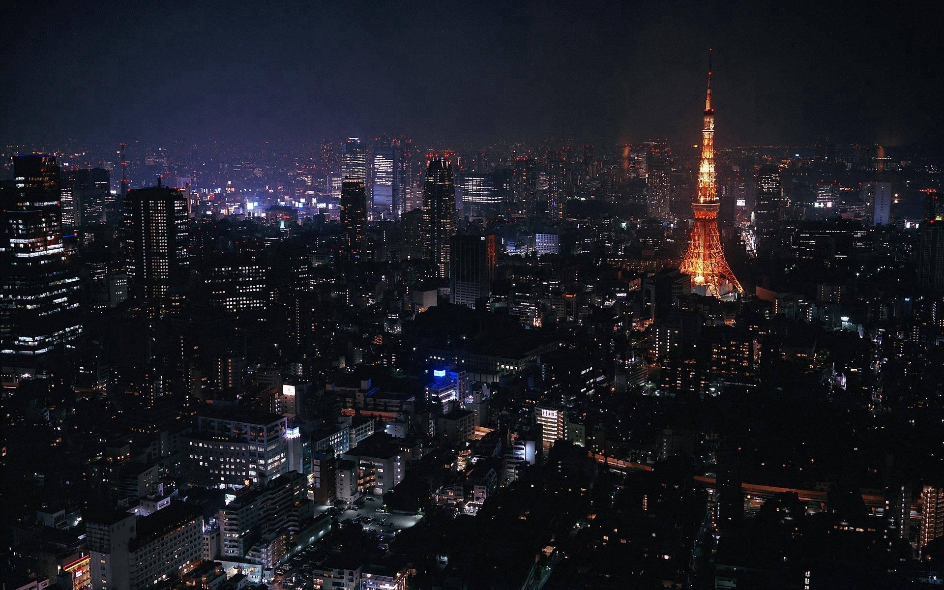 東京 桌布 壁紙 — 東京鐵塔在黑暗的天空中溫暖地發光，城市的燈光照亮了下方廣闊的城市景觀。