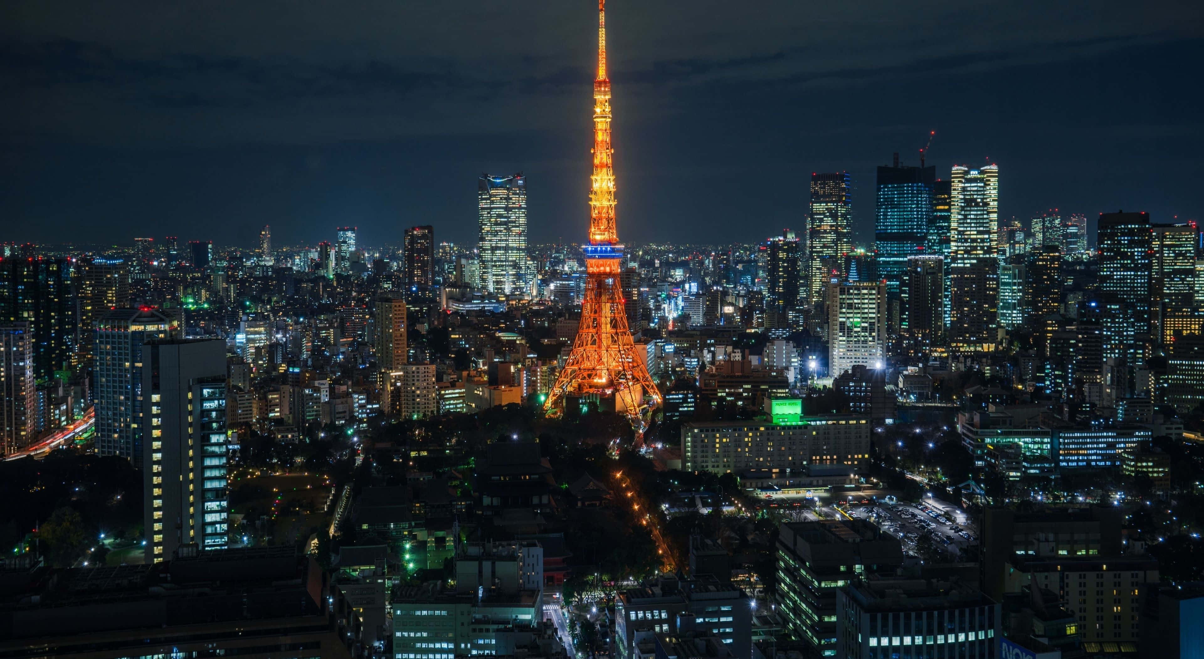 東京鐵塔 桌布 壁紙 — 東京鐵塔在黑暗的天空中溫暖地發光，城市燈光照亮了下方廣闊的城市景觀。