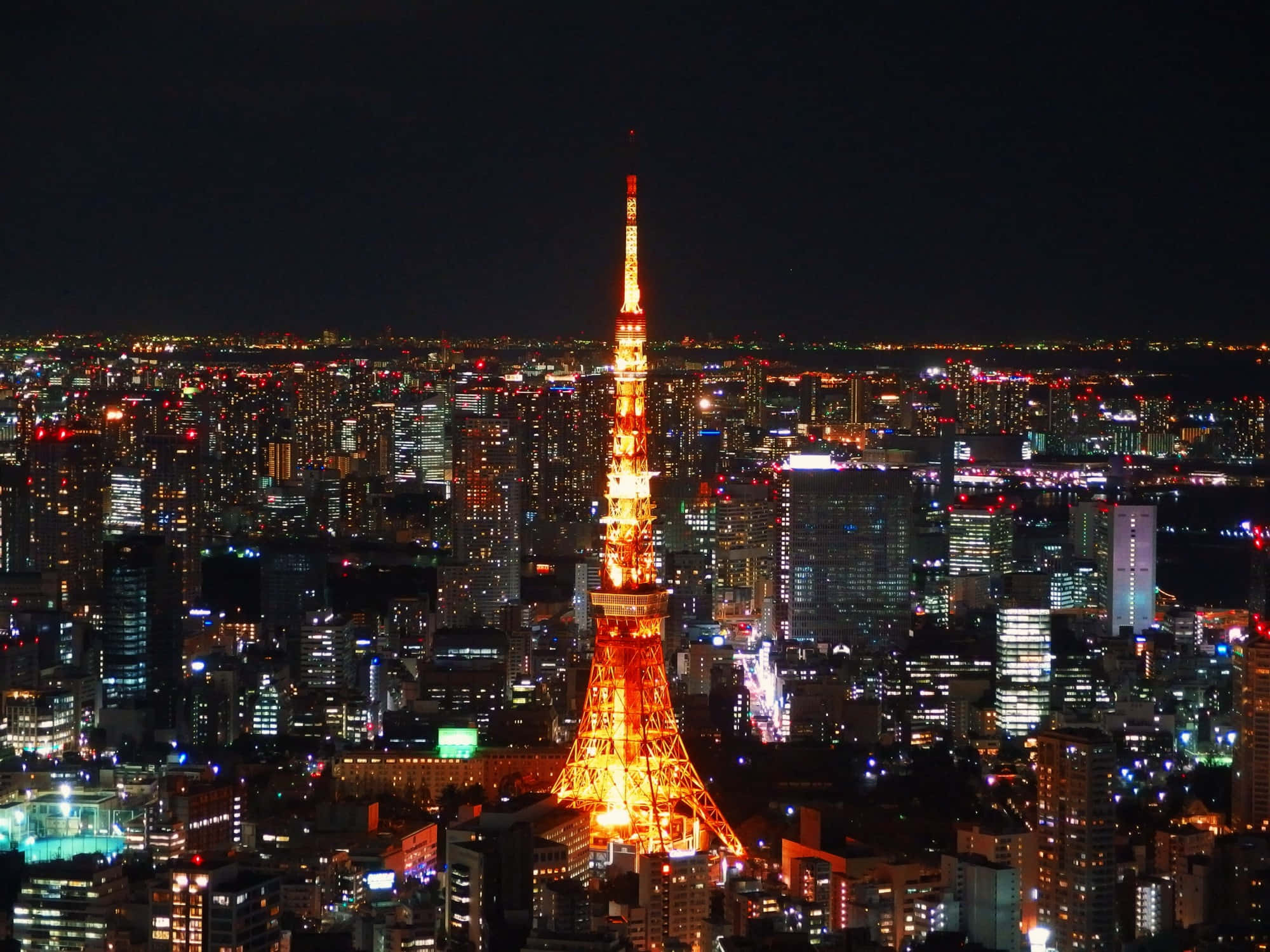 東京鐵塔 桌布 壁紙 — 東京鐵塔在黑暗的天空中溫暖地發光，用無數閃爍的燈光照亮下方廣闊的城市景觀。