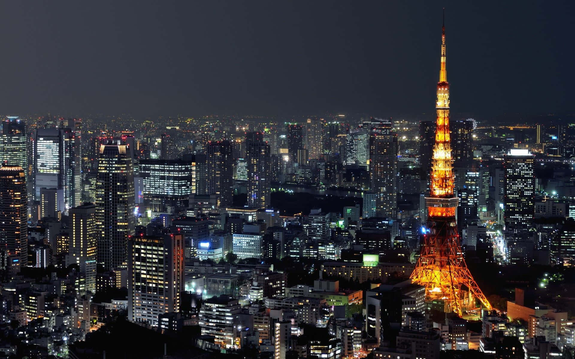 城市 桌布 壁紙 — 東京鐵塔在黑暗的天空中溫暖地發光，城市燈光照亮了下方廣闊的城市景觀。