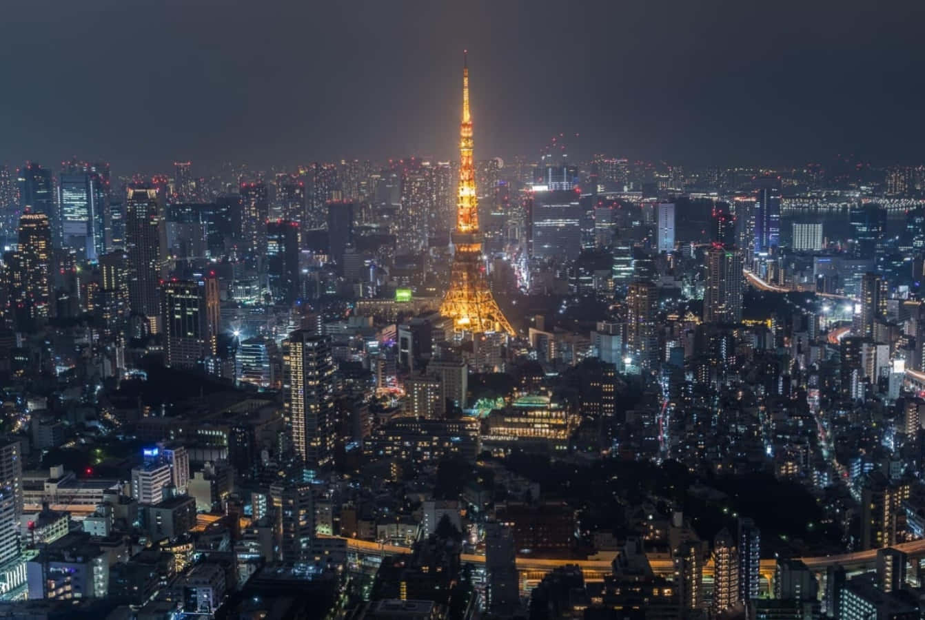 東京 桌布 壁紙 — 東京鐵塔在黑暗的天空中閃耀著金色光芒，城市的燈光照亮了下方廣闊的城市景觀。