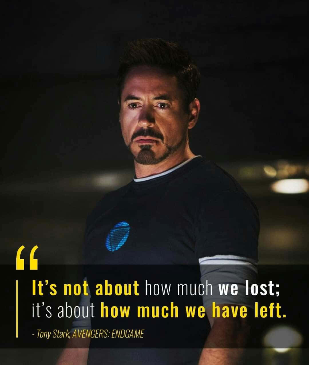 Iron Man Quotes 桌布 壁紙 — 東尼史塔克在昏暗場景中專注地凝視，身穿深色T恤，上有發光藍色弧形反應爐標誌。