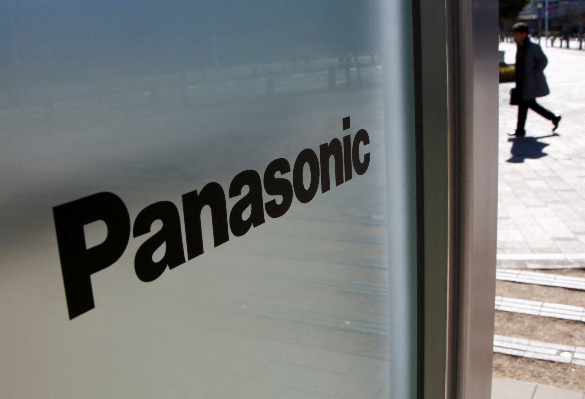 Panasonic 桌布 壁紙 — 松下標誌在磨砂玻璃上的特寫，一個模糊的行人在明亮的日光下走過。