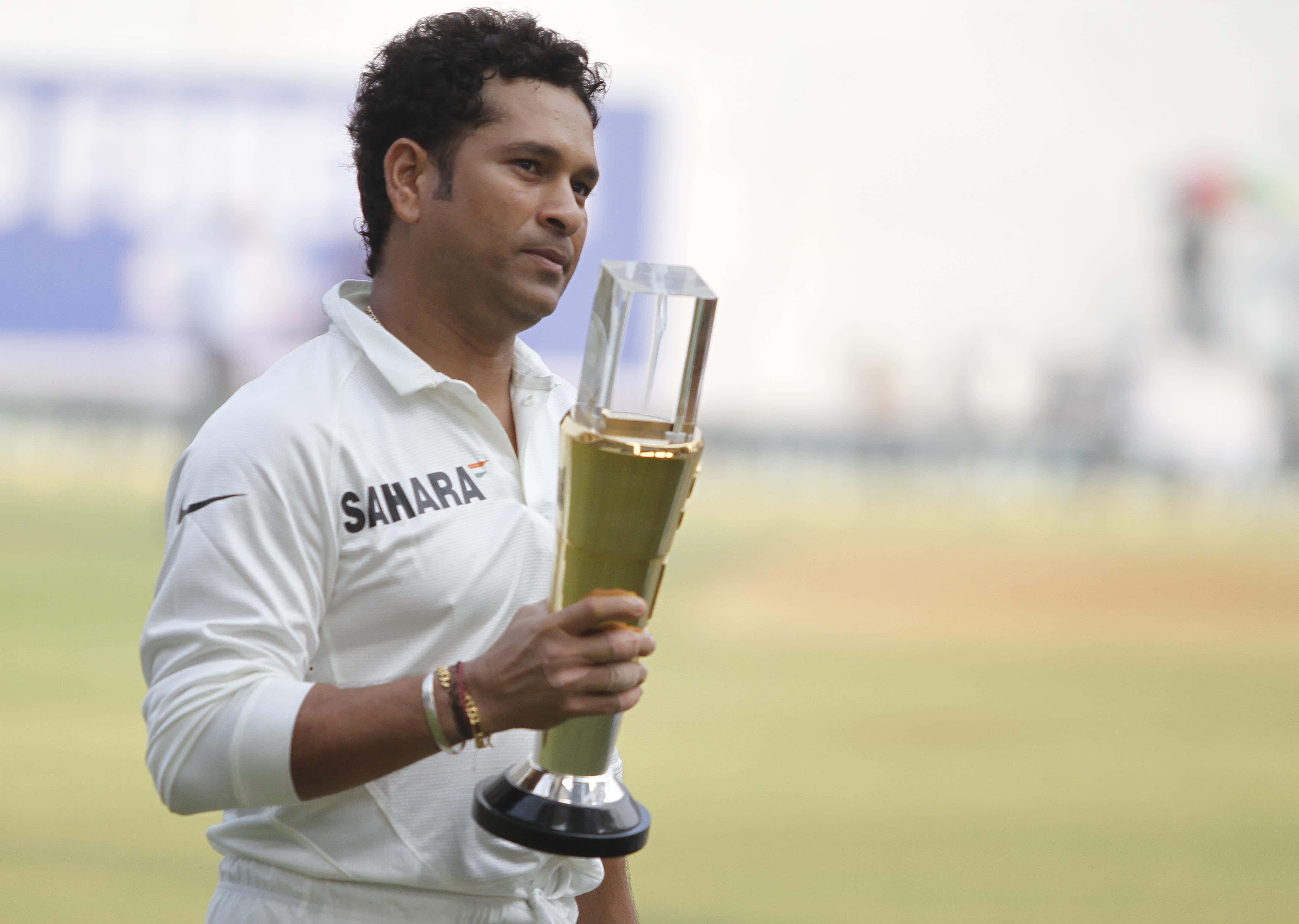 Sachin Tendulkar 桌布 壁紙 — 板球傳奇人物沙欽·坦杜卡在陽光明媚的綠色球場上，身穿白色Sahara球衣，手持閃閃發光的獎盃。