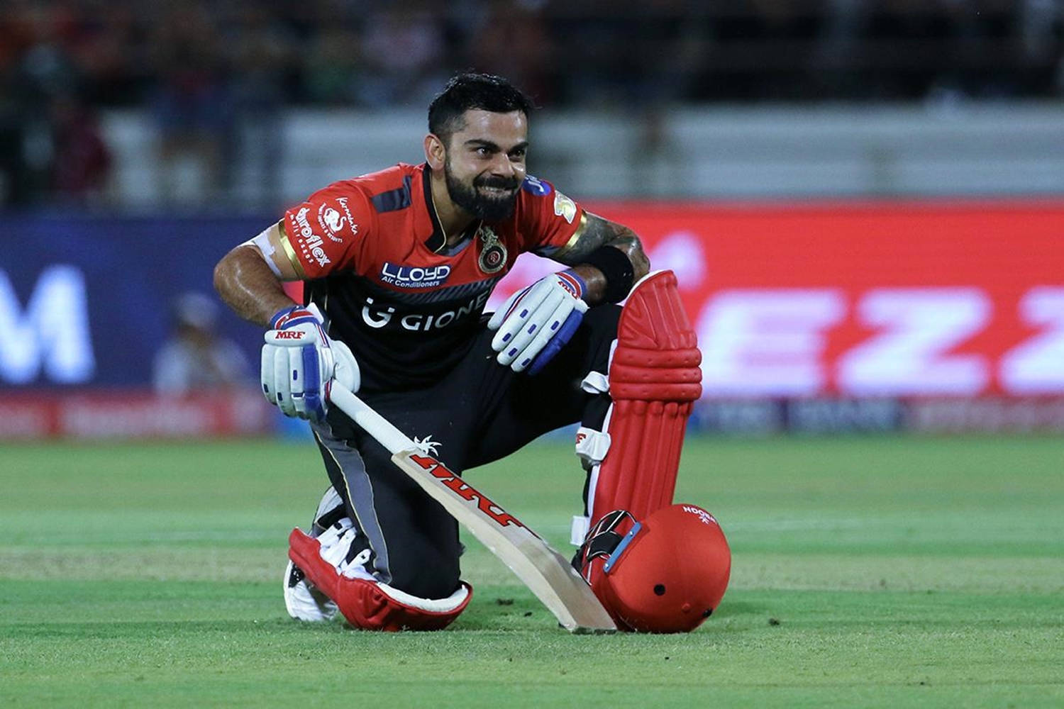 royal challengers bangalore 桌布 壁紙 — 板球運動員 Virat Kohli 在夜間比賽中，在球場燈光下跪在草地上，手持球棒，頭盔放在身旁。
