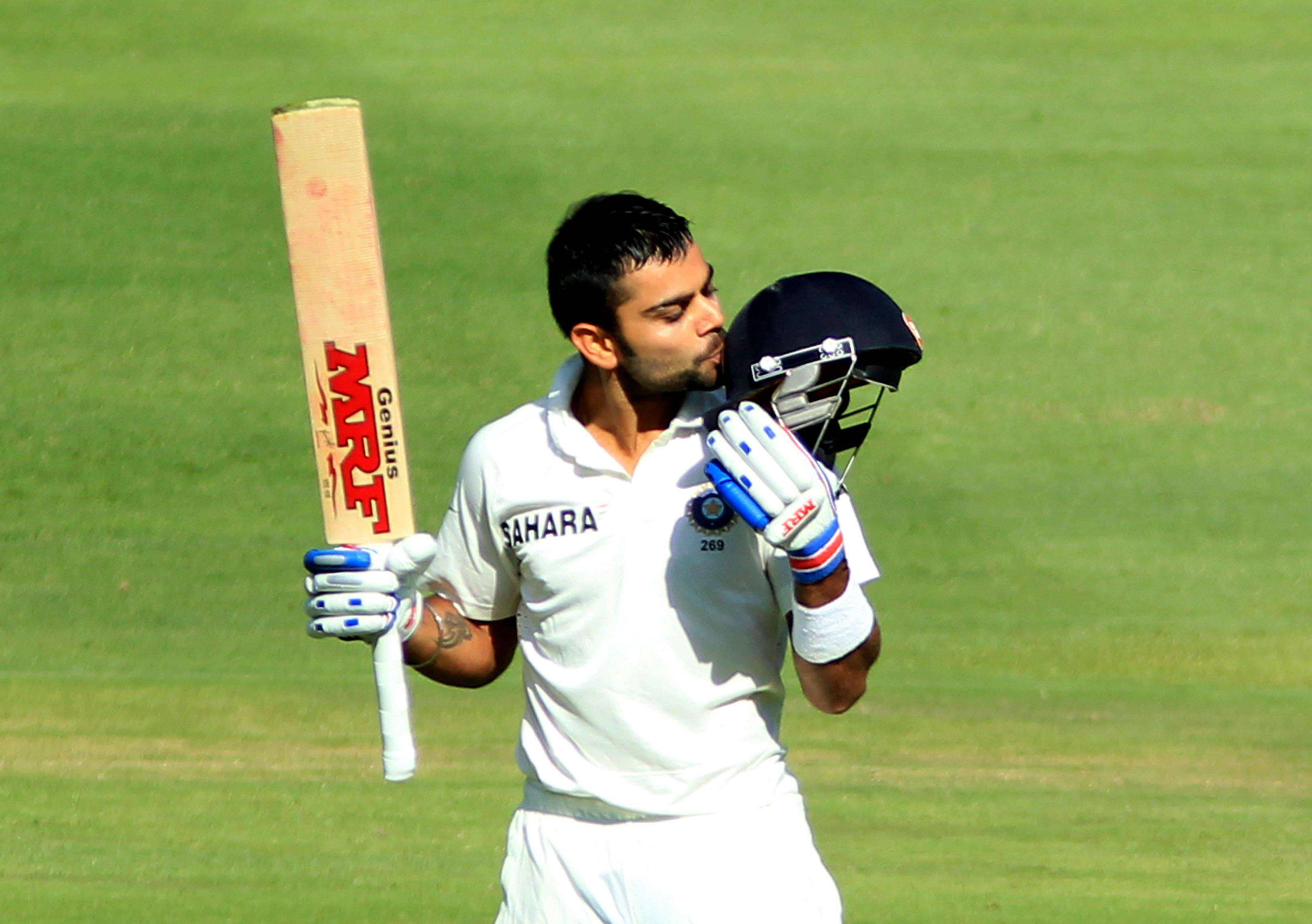 royal challengers bangalore 桌布 壁紙 — 板球運動員 Virat Kohli 身穿白色制服，在陽光明媚的綠色場地上手持球棒和頭盔。