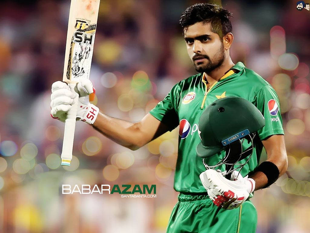 Babar 桌布 壁紙 — 板球運動員Babar Azam身穿綠色制服，在球場燈光下手持球棒和頭盔，背景是模糊的人群。