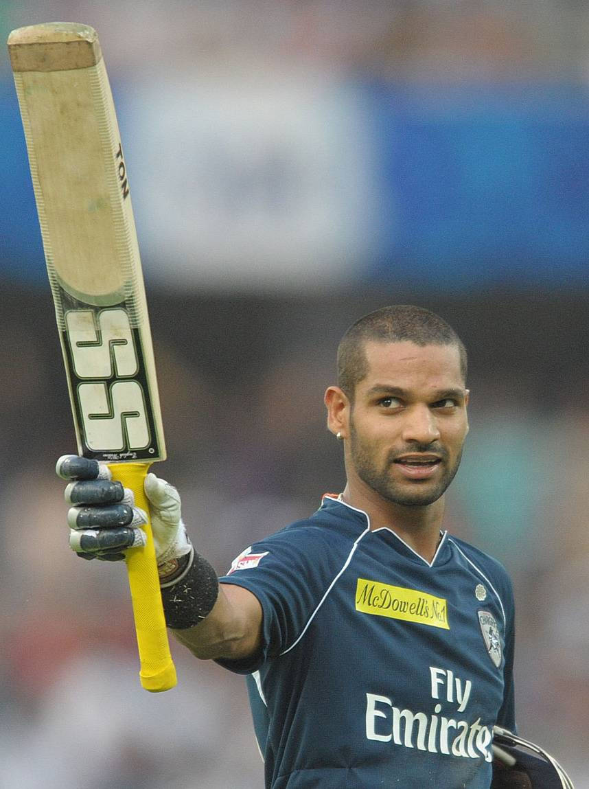 shikhar dhawan 桌布 壁紙 — 板球運動員在球場燈光下的比賽中，自豪地舉起球棒，表情專注。